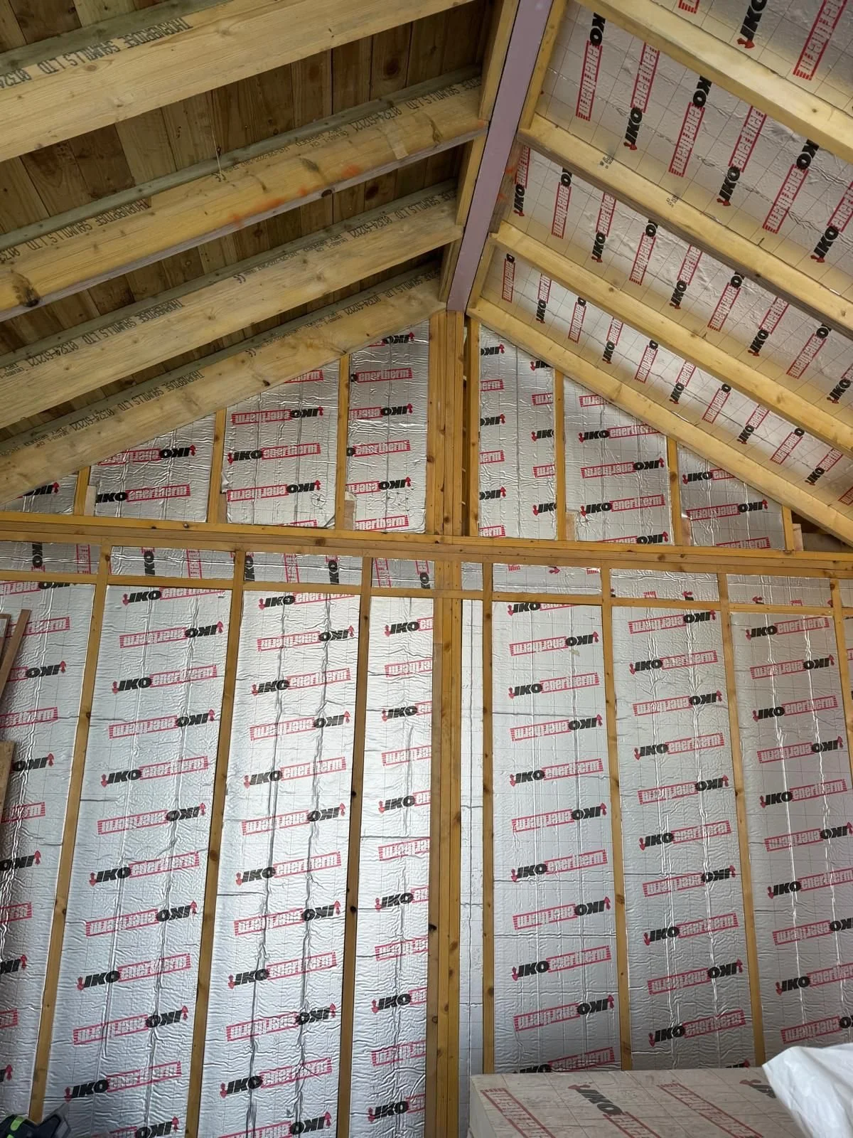 The interior of a building under construction, showing wooden framing and metal insulation panels on walls and ceiling.
