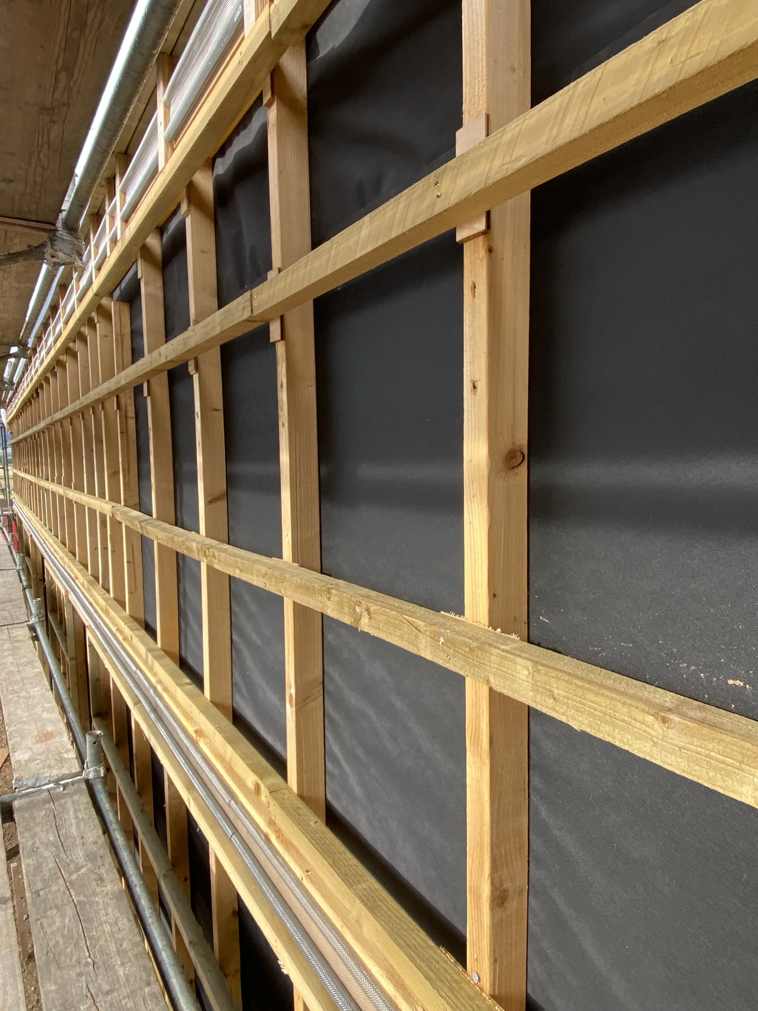 Interior of a building under construction showing wooden wall framing and black weather-resistant barrier material.