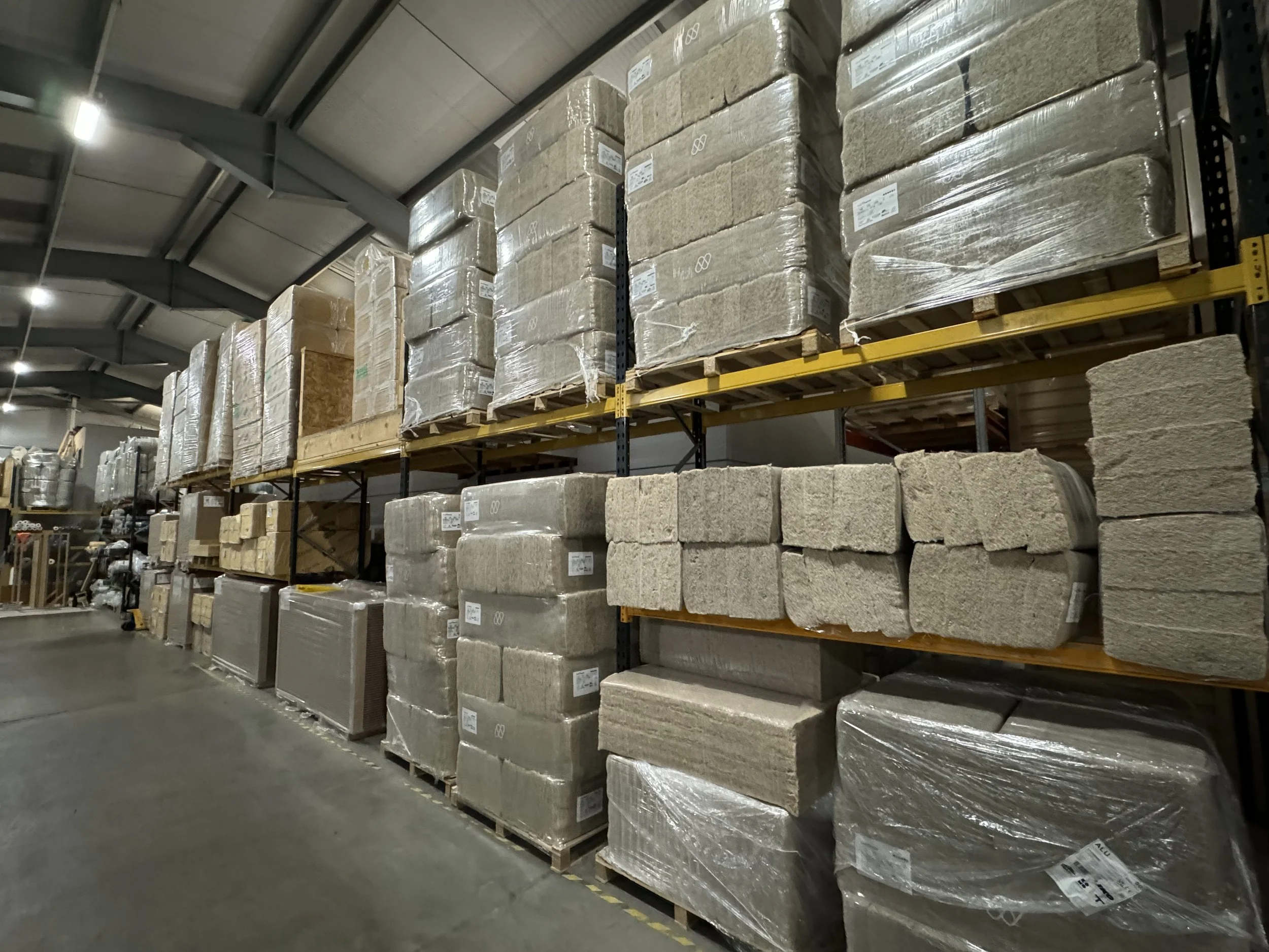 Warehouse aisle with shelves stacked with wrapped construction materials, including stone or brick blocks, and pallets.