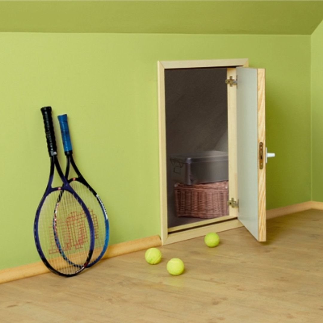 Two tennis rackets leaning against a green wall, three tennis balls on the floor, and an open small cabinet with a storage box and wicker basket inside.