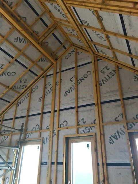 Interior view of a building under construction, showing wooden framing and insulation installed on the walls and ceiling.