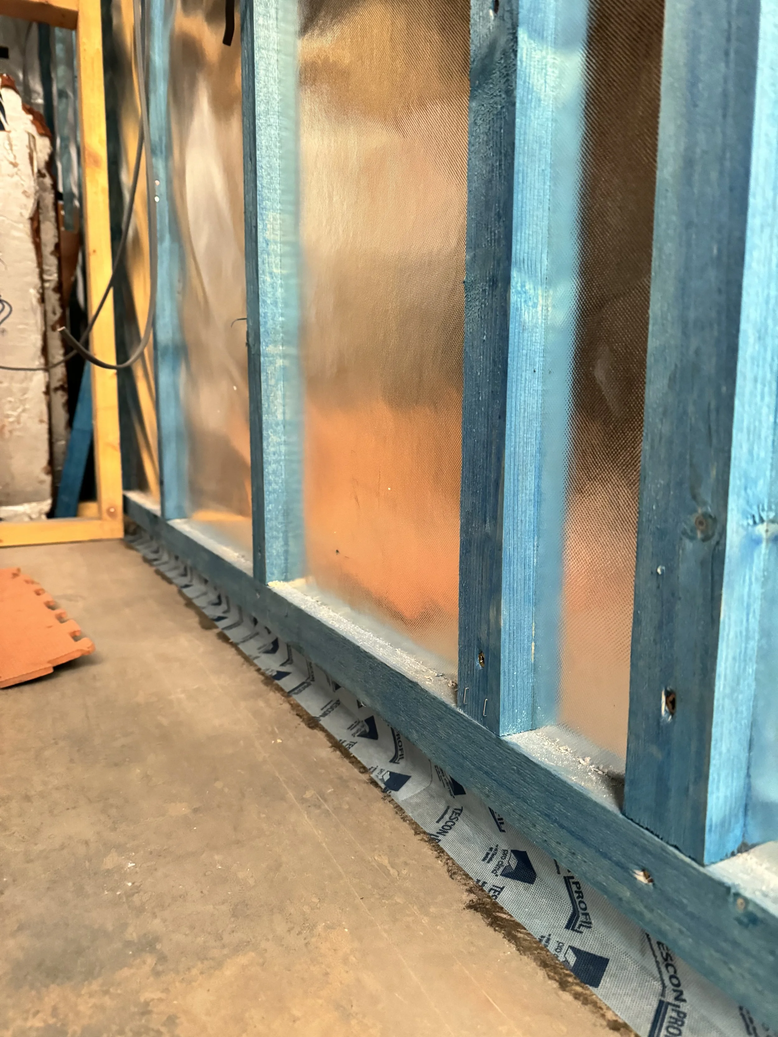 Close-up of an interior building wall under construction, showing blue wooden framing, insulation material, and some wiring.