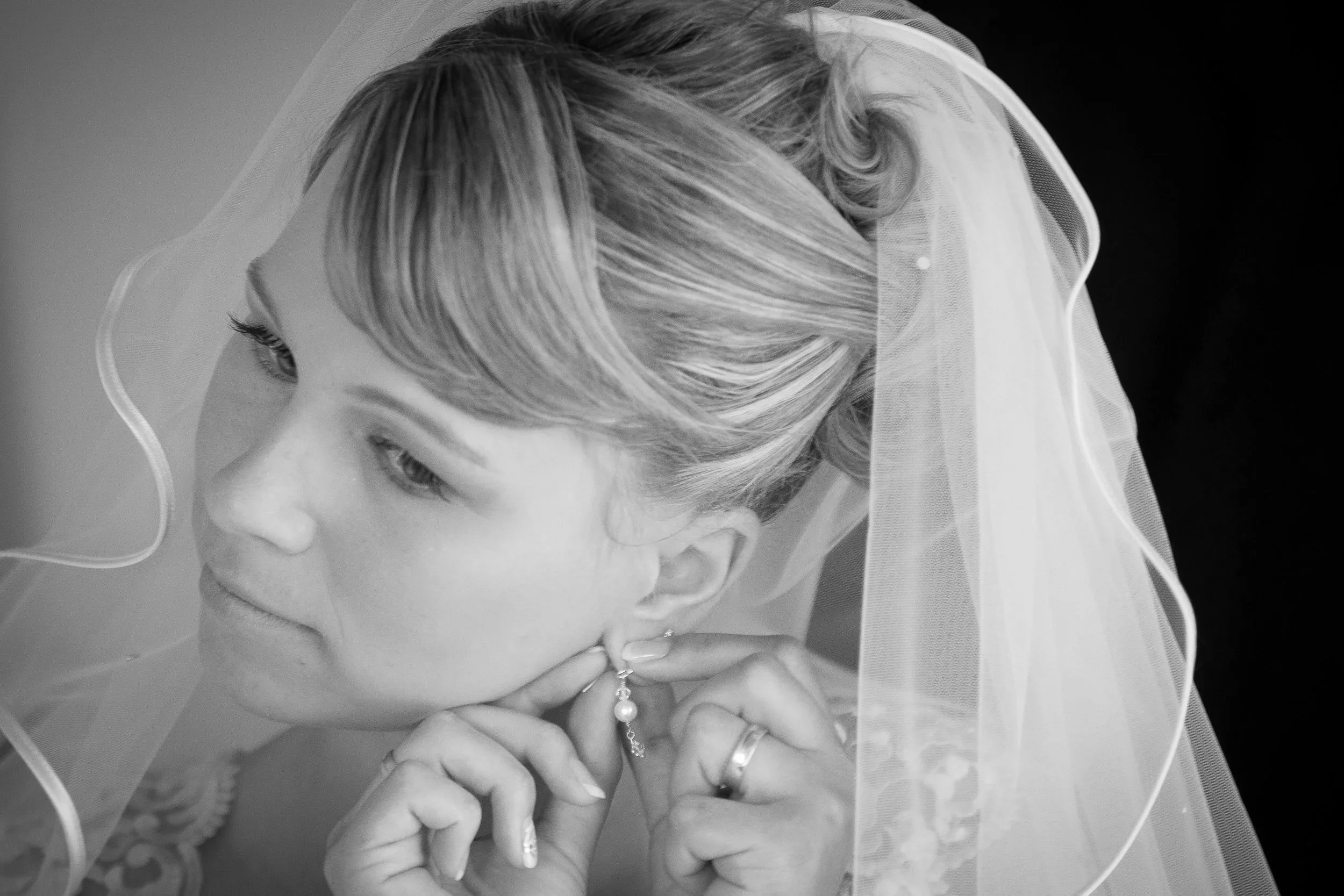Frau mit Schleier beim Hochzeitsvorbereitungen, öffnet eine Perlenohrring, Nahaufnahme in Schwarz-Weiß