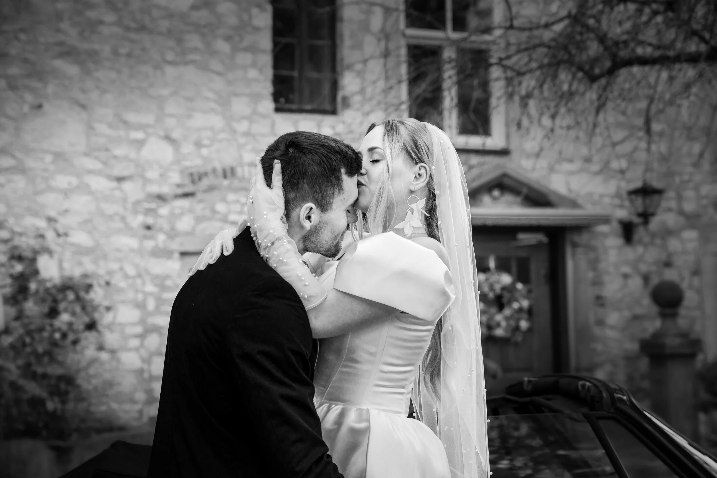 Braut und Bräutigam auf ihrem Hochzeitstag, die sich innig küssen, vor einem alten Steingebäude in Italien , schwarz-weiß Aufnahme.