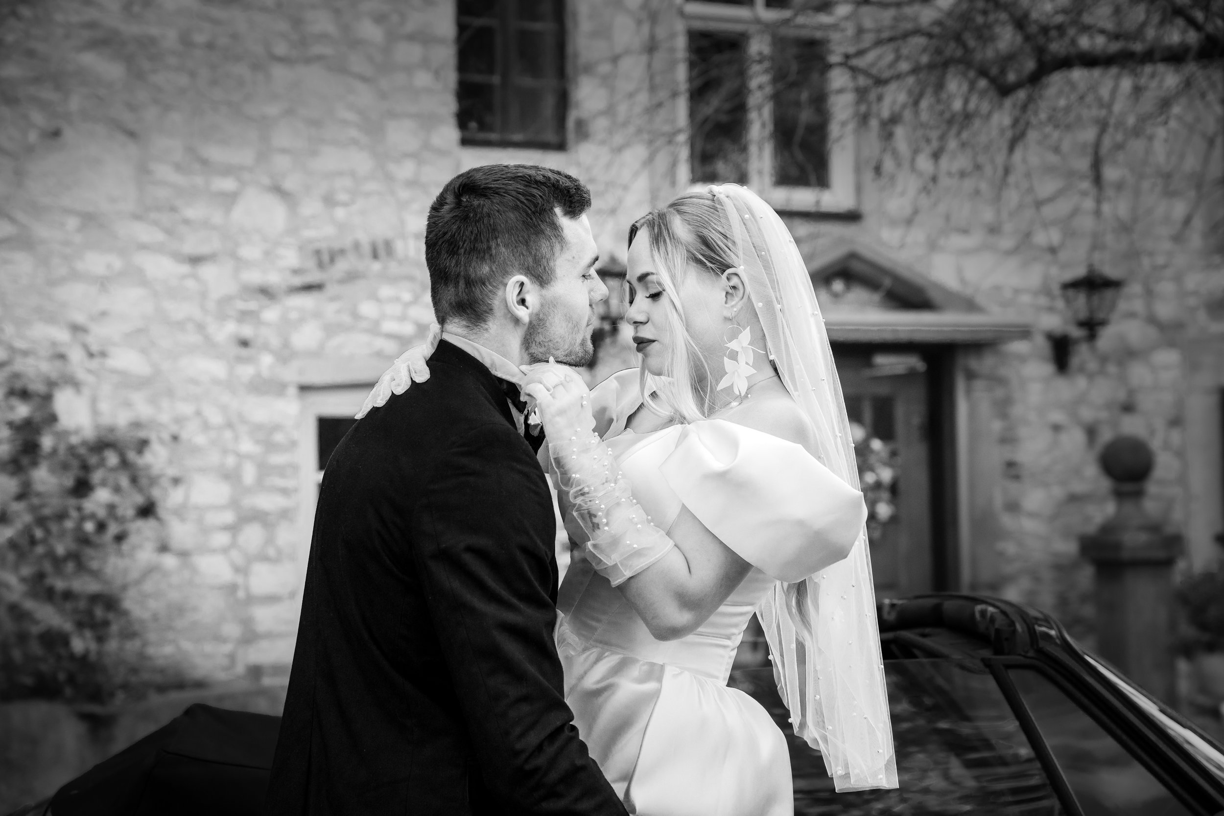 Ein Brautpaar bei einer Hochzeit, das sich nahekommt, im schwarzen und weißen Foto, vor einer alten Steinmauer in Italien.