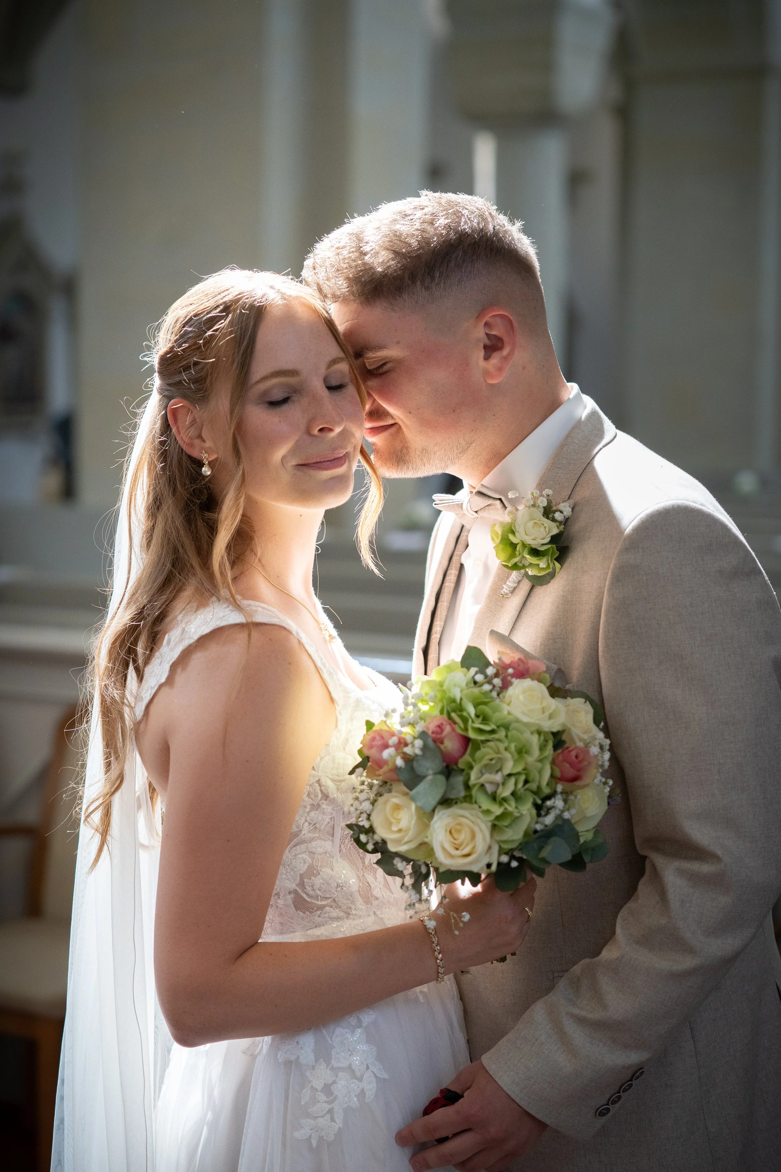 Ein Brautpaar in einer Kirche, das sich anfühlt und lächelt, mit der Braut, die einen Blumenstrauß hält.