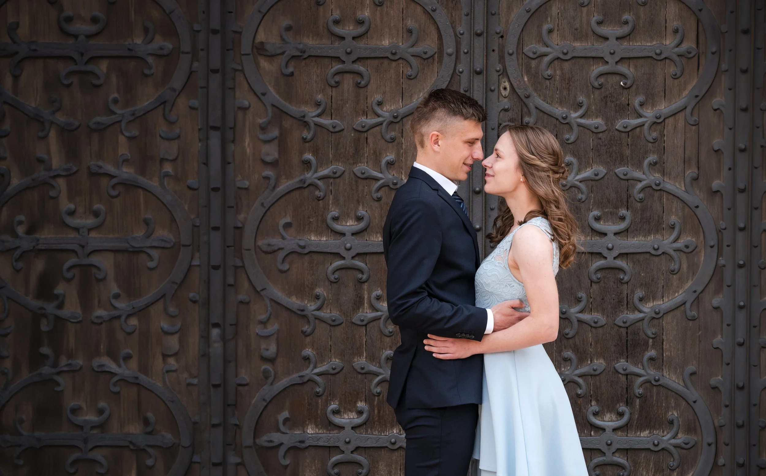 Ein Paar in Hochzeitskleidung steht sich vor einer geschnitzten Holztür gegenüber, blickt sich verliebt an in Braunschweig.