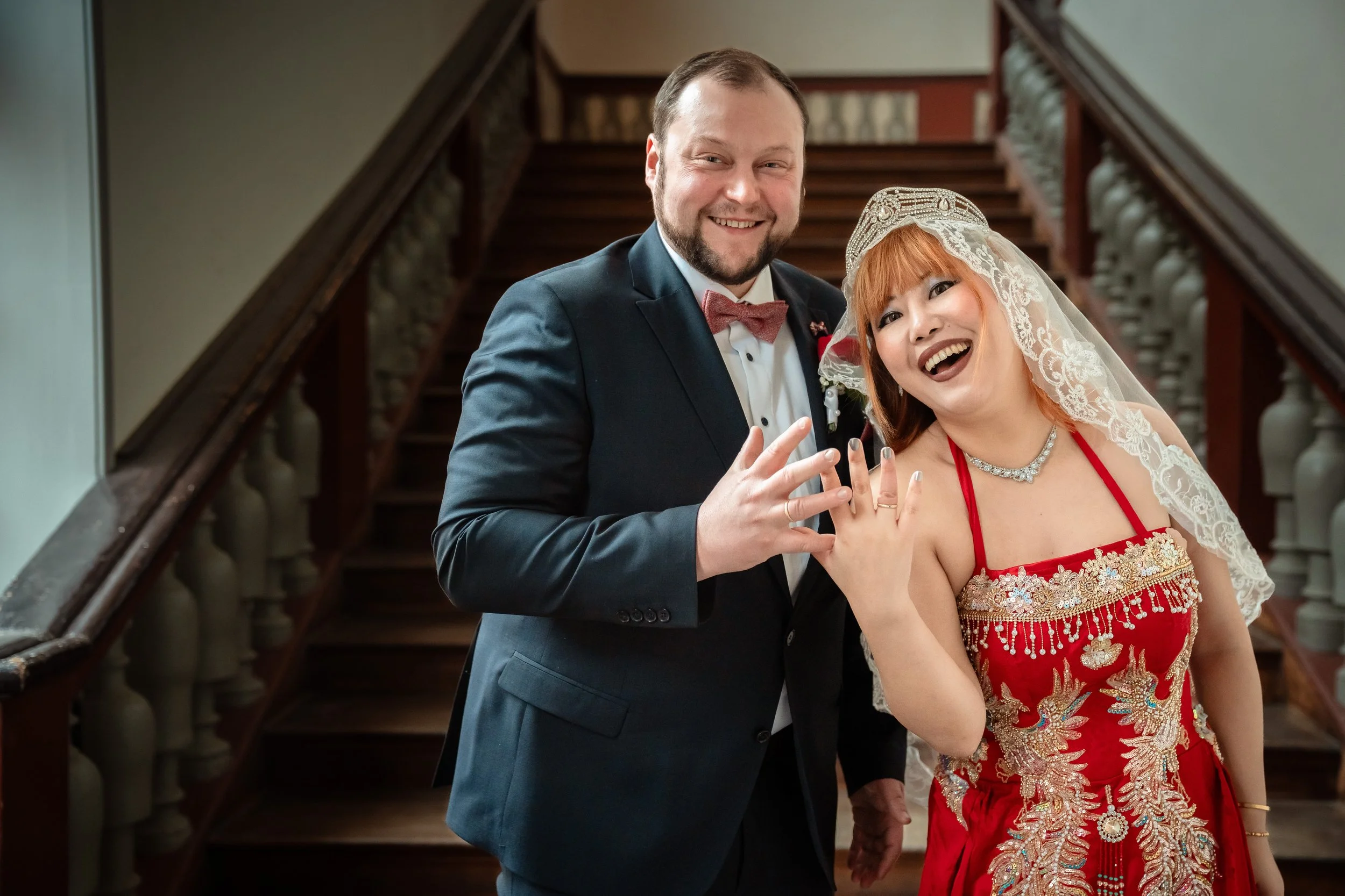 Ein glückliches Brautpaar zeigt ihre Eheringe auf einer Treppe im Hochzeitssaal.