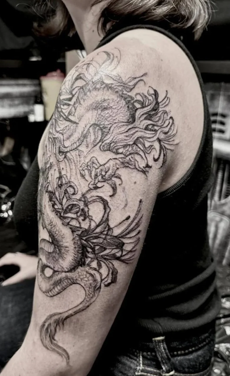 Black and grey dragon tattoo on upper arm and shoulder, featuring a detailed East Asian-style dragon with scaled body, flowing mane and whiskers, and dynamic swirling composition. Fine line and shading work. Fresh tattoo, Siren Tattoo Studio, Lucerne