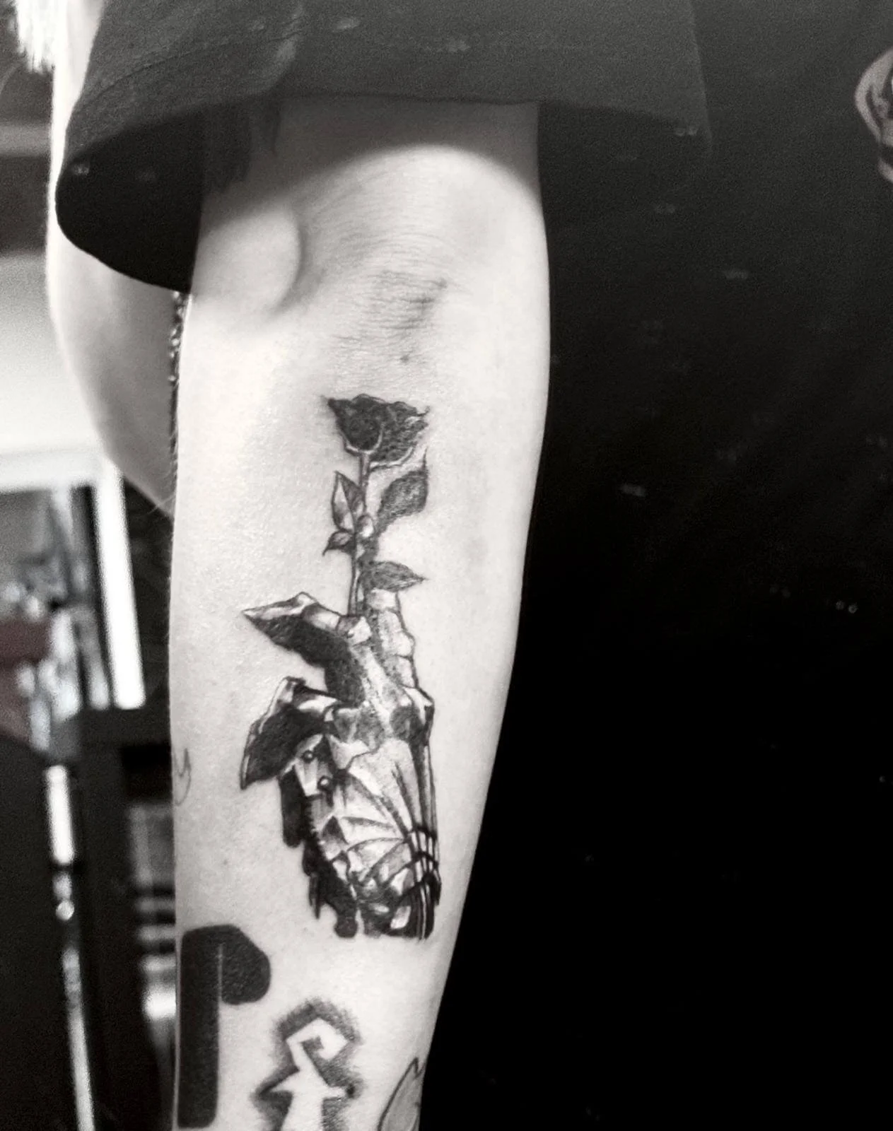 Blackwork illustrative forearm tattoo — skeleton gauntlet hand holding a dark rose stem in black and grey linework by Siren Tattoo Lucerne