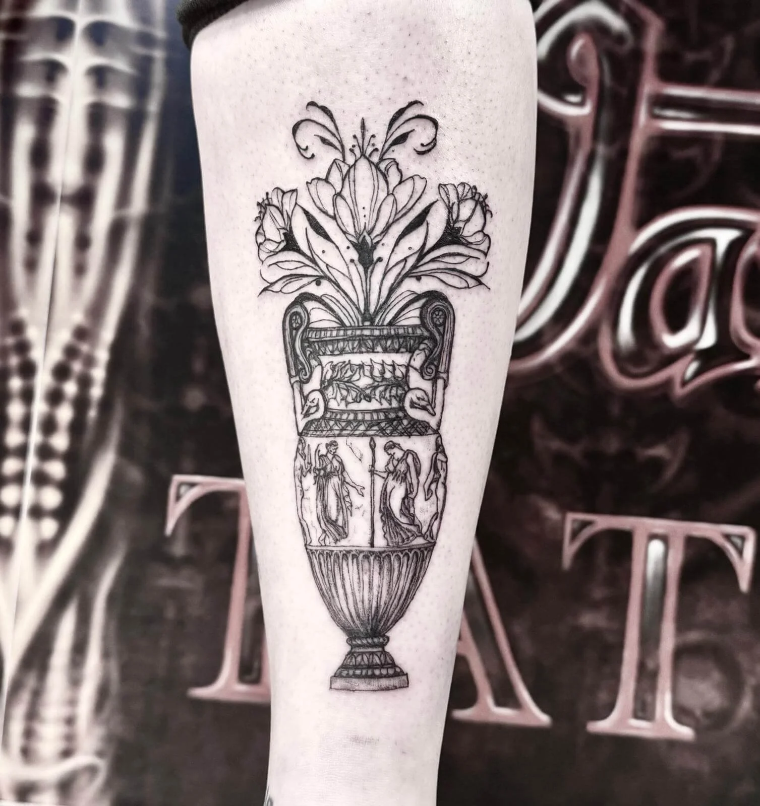 Fine-line illustrative forearm tattoo — ornate Greek amphora vase with classical figures, lily blooms and botanical flourishes in black and grey by Siren Tattoo Lucerne