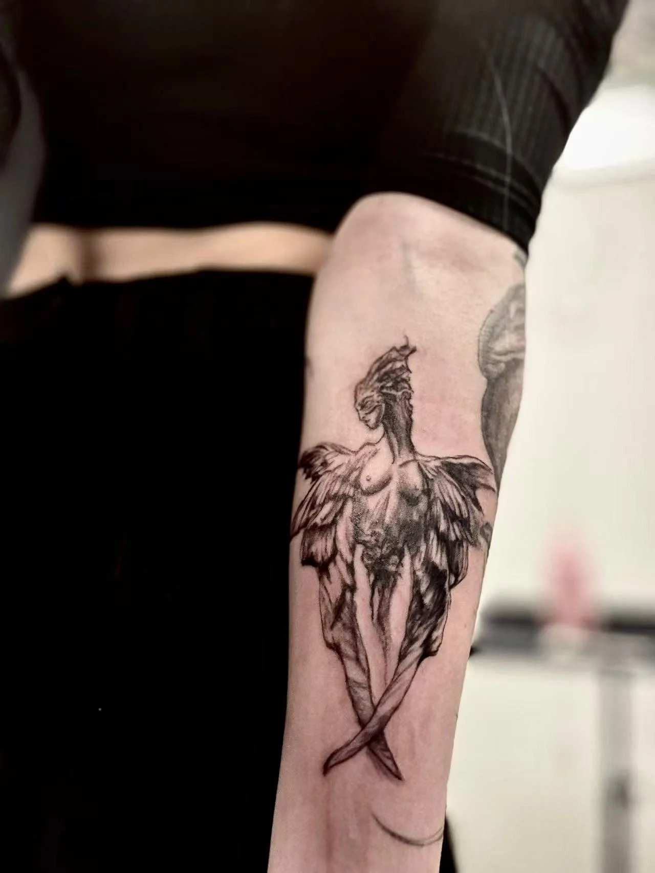 Fine-line illustrative siren tattoo on forearm — winged mythological female figure in black and grey by Siren Tattoo, Lucerne