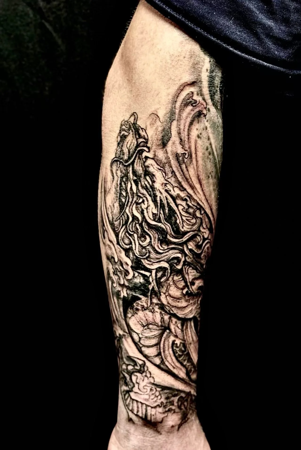 Dark illustrative dragon sleeve tattoo — flowing blackwork dragon with waves and mask on full forearm by Siren Tattoo Lucerne