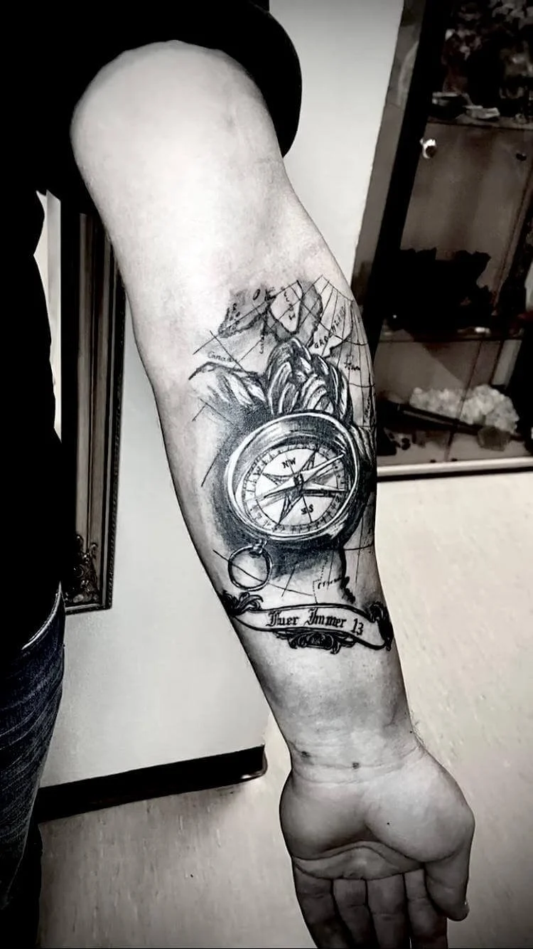 Realism forearm tattoo — hyperdetailed vintage compass with map, mountain and banner script reading "Fuer Immer 13" in black and grey by Siren Tattoo Lucerne