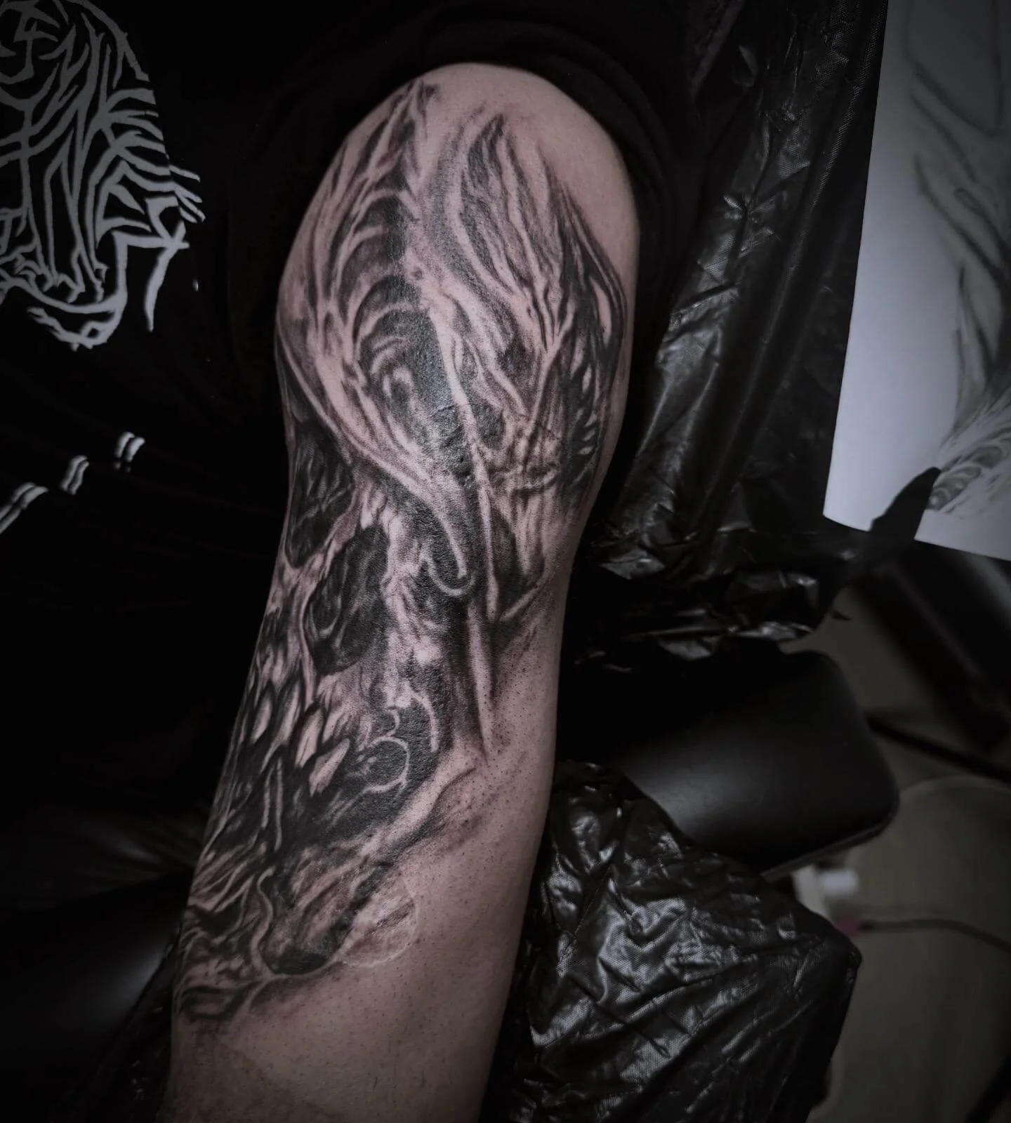 Dark realism half-sleeve tattoo fresh — hooded skull with organic shredded texture in deep black and grey by Siren Tattoo Lucerne