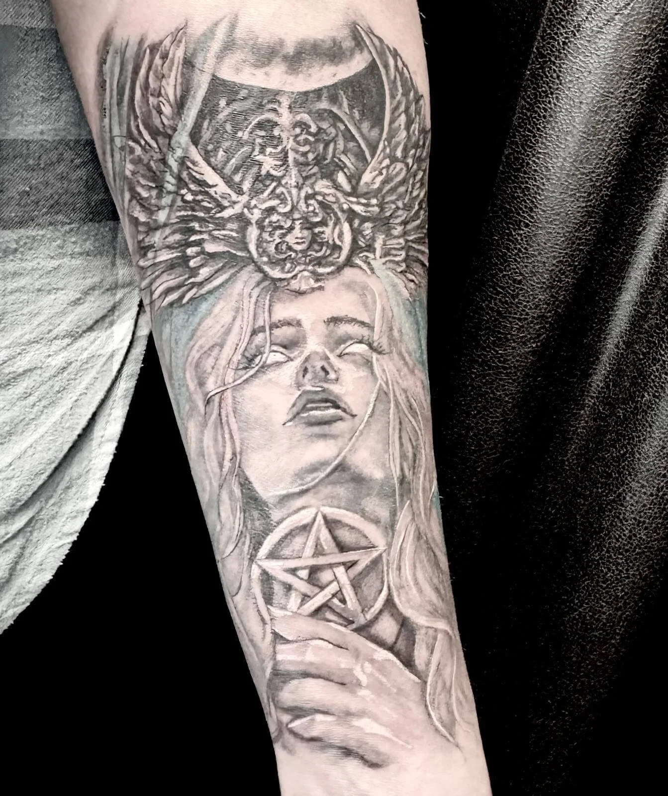 Black and grey realism forearm tattoo — dark goddess portrait with winged crown, pentagram and crescent moon in illustrative style by Siren Tattoo Lucerne