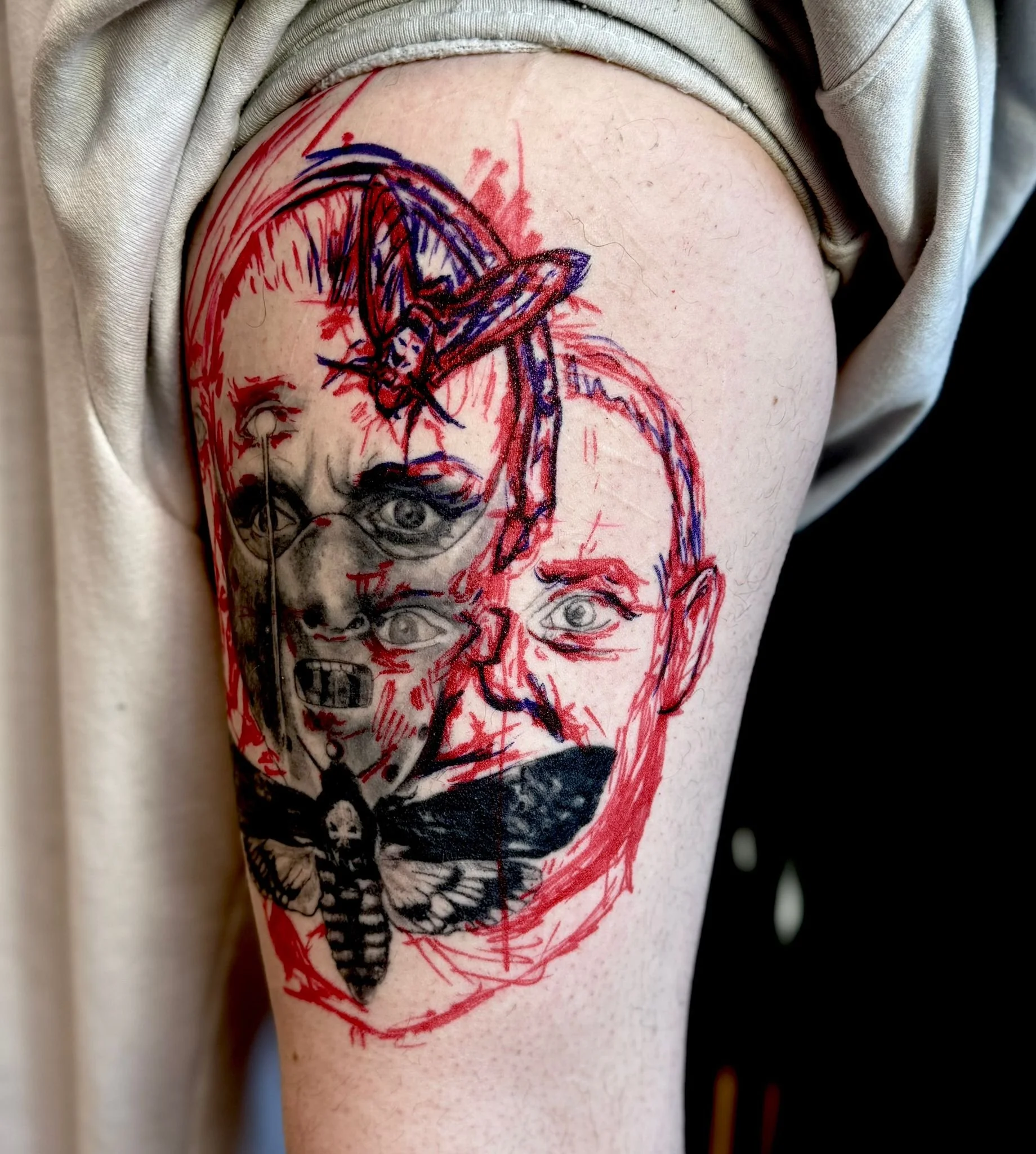 Illustrative freehand tattoo on upper arm — split-face Hannibal Lecter portrait with death's-head moth and red sketch linework by Siren Tattoo Lucerne