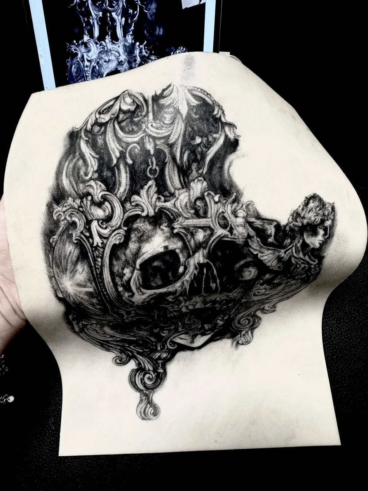Close-up practice piece on fake skin — baroque skull with acanthus scrollwork and ornate pendant detail, large format design by Siren Tattoo Lucerne