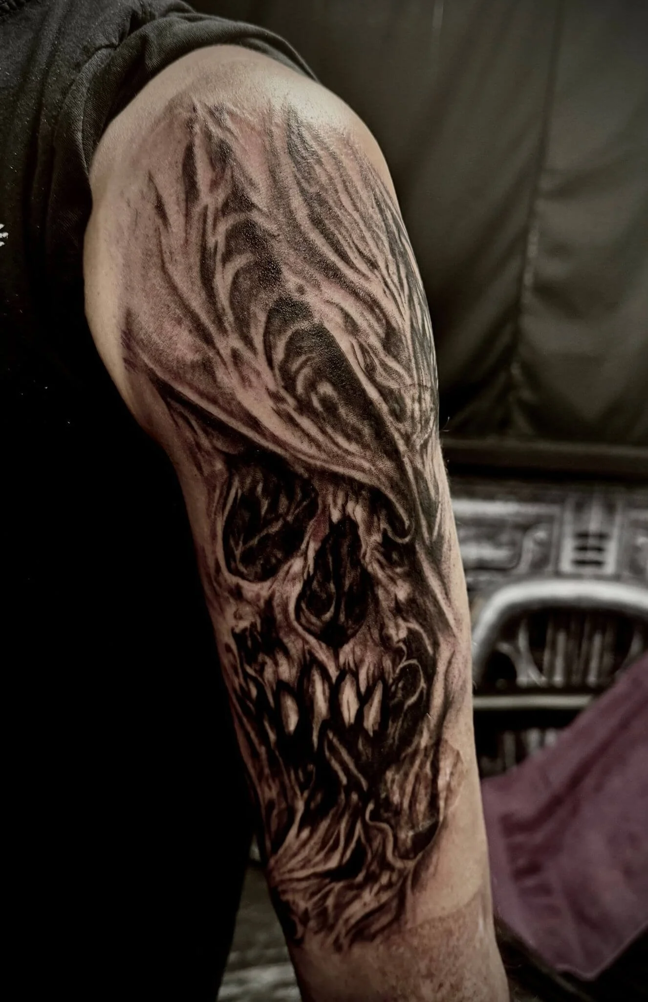 Dark realism half-sleeve tattoo — hooded skull with shredded flesh texture in deep black and grey by Siren Tattoo Lucerne