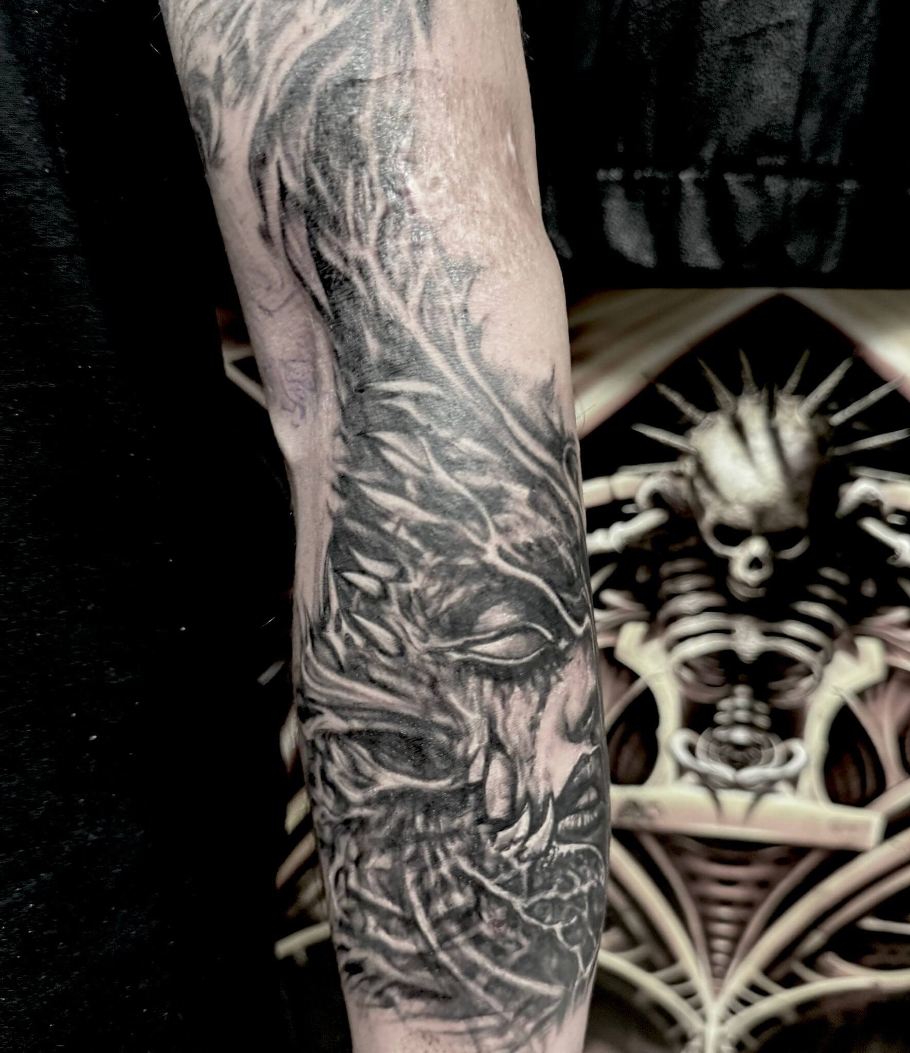 Black and grey realism forearm tattoo — female face emerging from dark organic texture and feathers by Siren Tattoo Lucerne