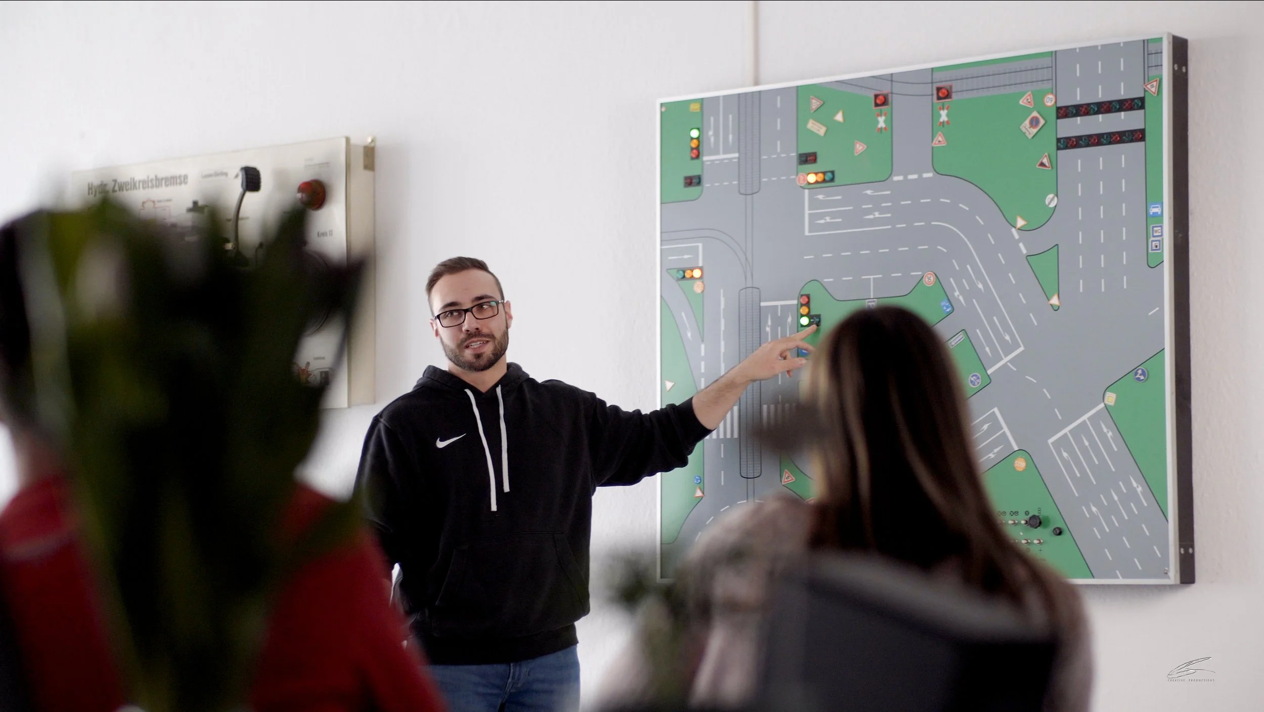 Ein Mann erklärt einer Gruppe Menschen eine Verkehrssimulation an einer Wandtafel in einem Unterrichtsraum.