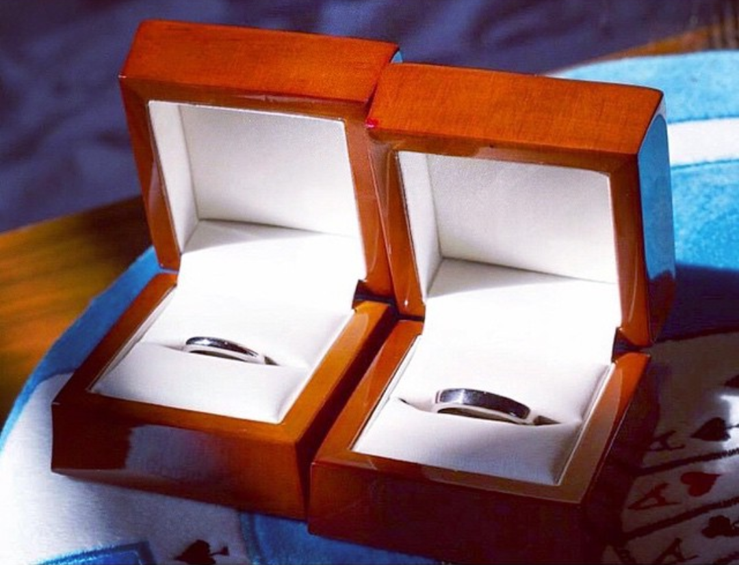 Two silver rings in open wooden jewelry boxes on a blue surface.