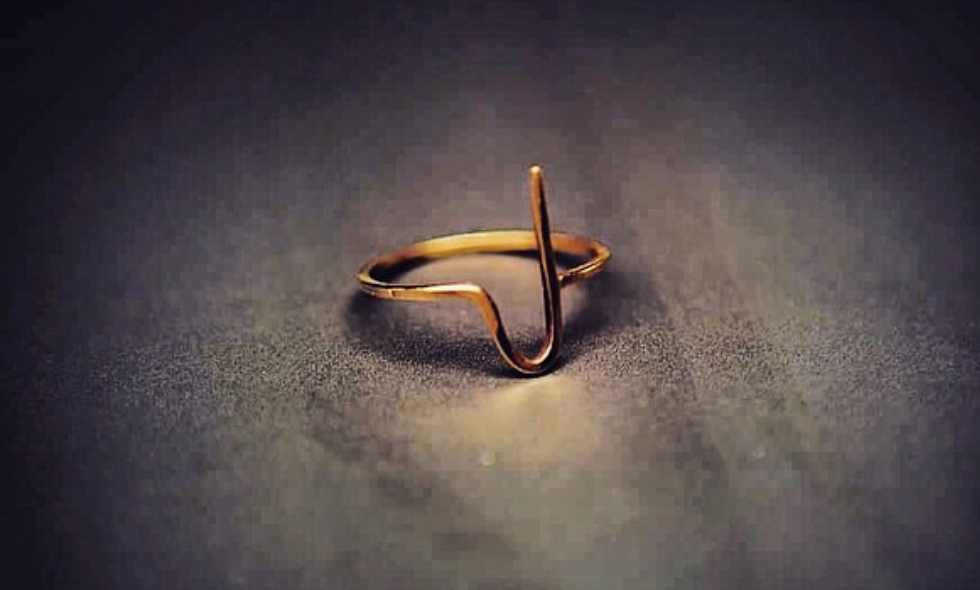 A gold ring shaped like a heart with an EKG heartbeat line design on a dark surface.
