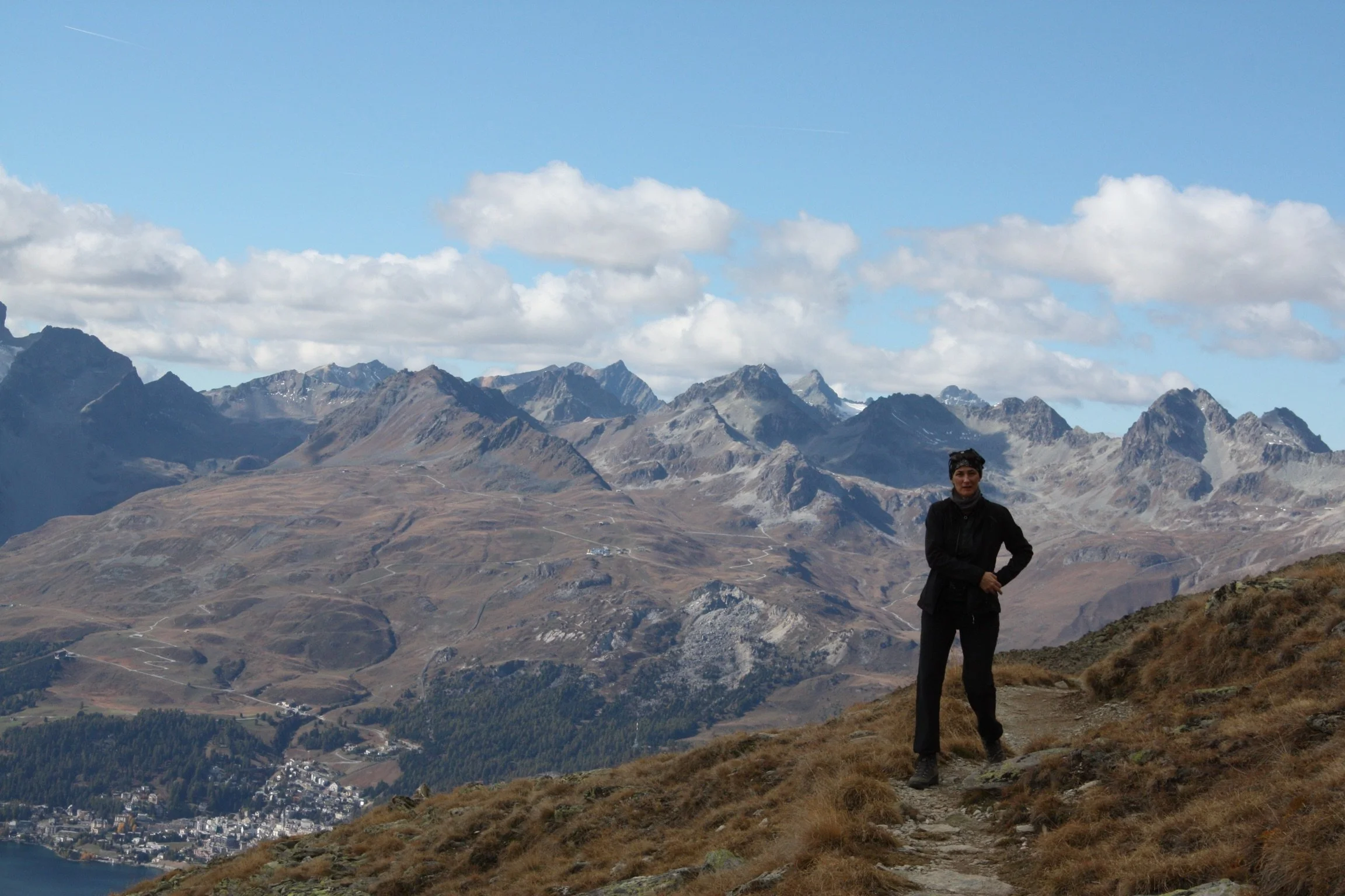 Fabienne Lämmler steht auf einem Wanderweg in den Bergen, umgeben von anspruchsvollen Gipfeln und bewölktem Himmel.