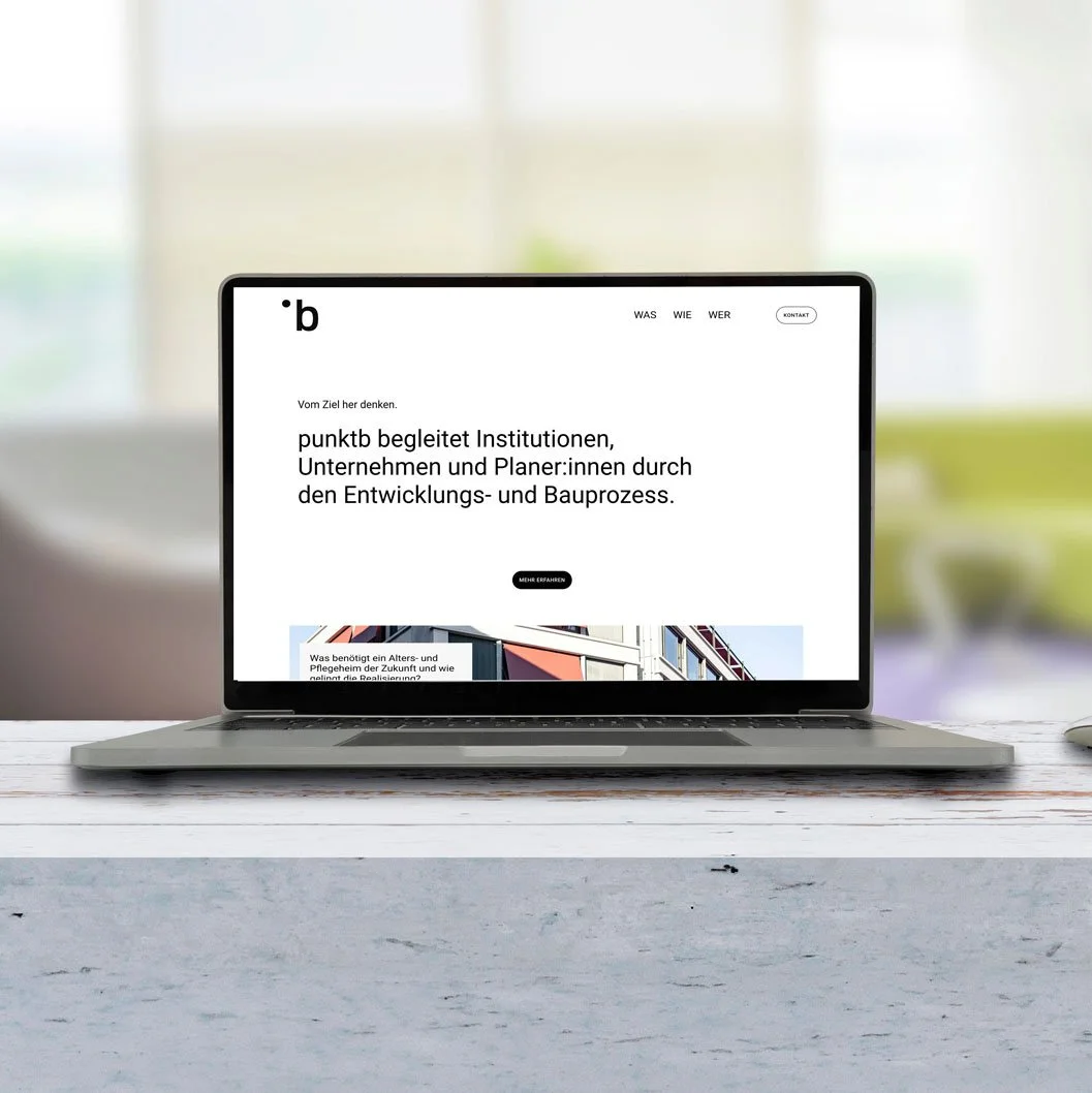 Laptop auf einem weißen Tisch zeigt eine Webseite mit deutschem Text, die Organisation punktb beschreibt, die Institutionen, Unternehmen und Planer durch Entwicklungs- und Bauprozesse begleitet.