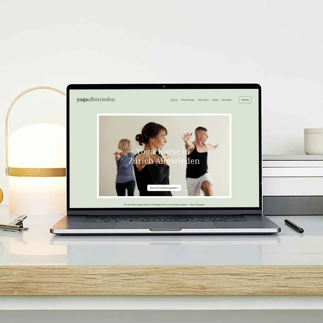Laptop auf einem weißen Schreibtisch zeigt eine Webseite für Yoga-Kurse in Zürich Albistrieden, mit Bild von Menschen beim Yoga.