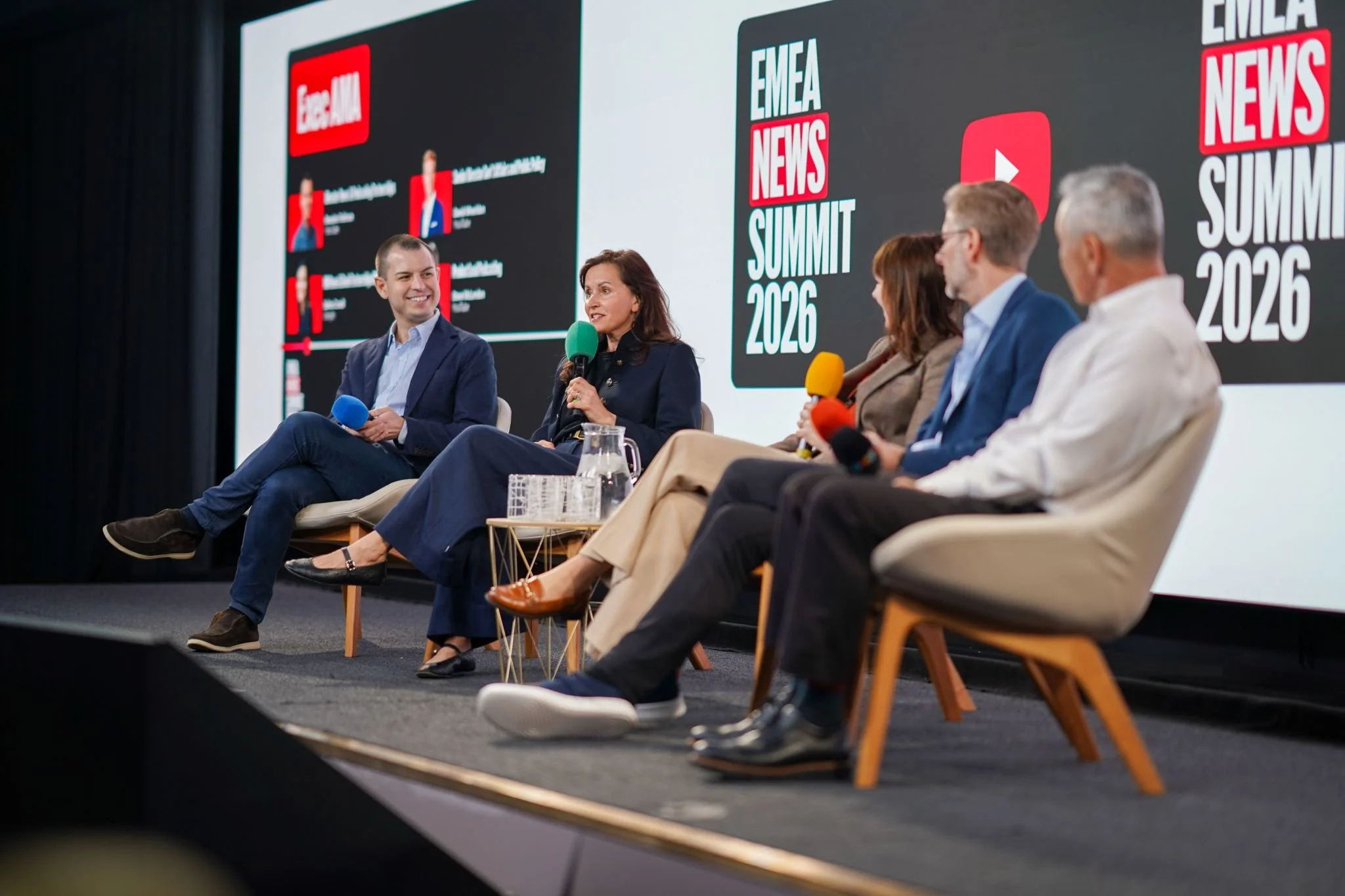Panel of five people sitting on stage at the Google News Summit 2026, engaged in a discussion, with a large screen behind them displaying the event's logo and title.