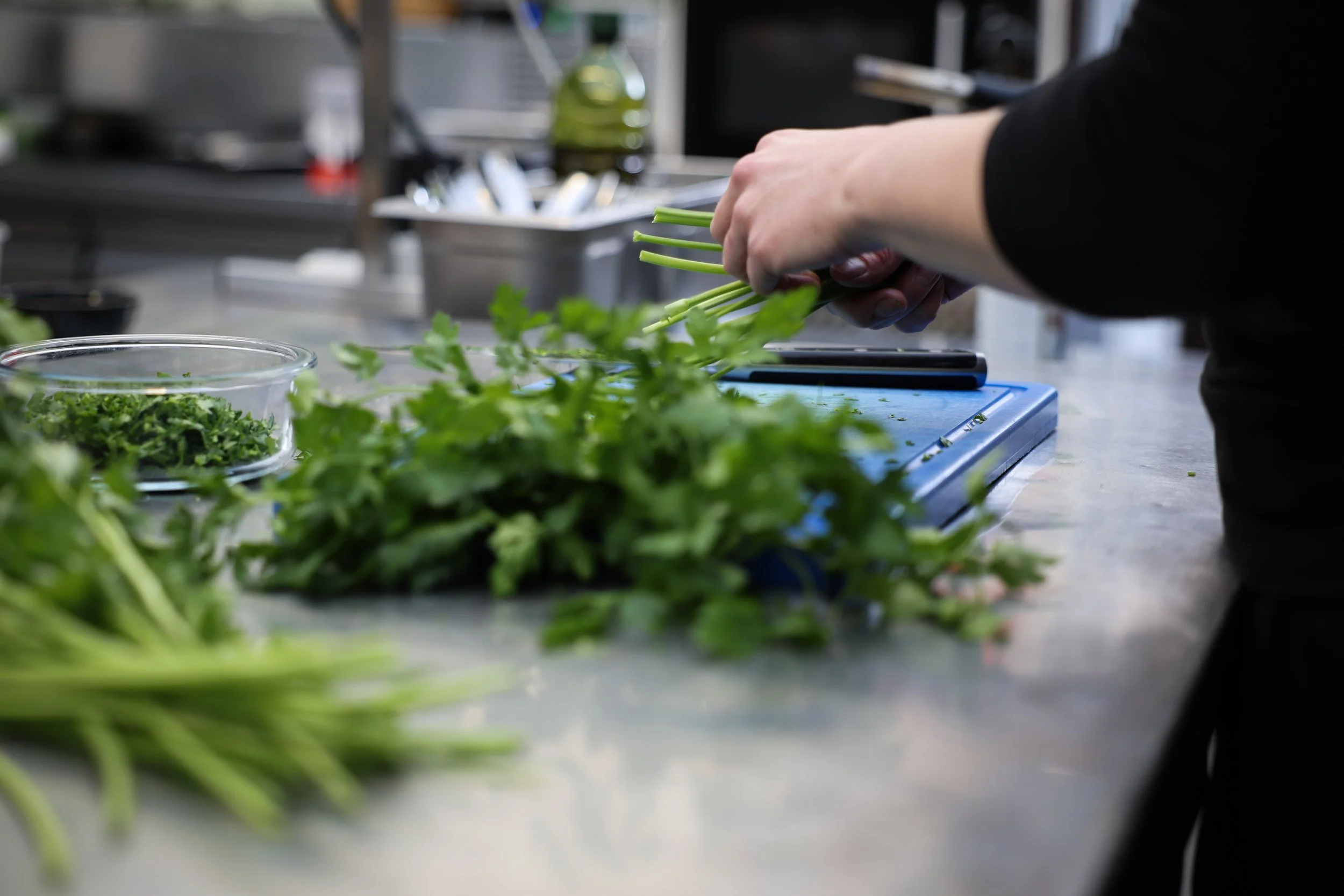 Persoon die verse groene kruiden snijdt op een blauwe snijplank in een professionele keuken.