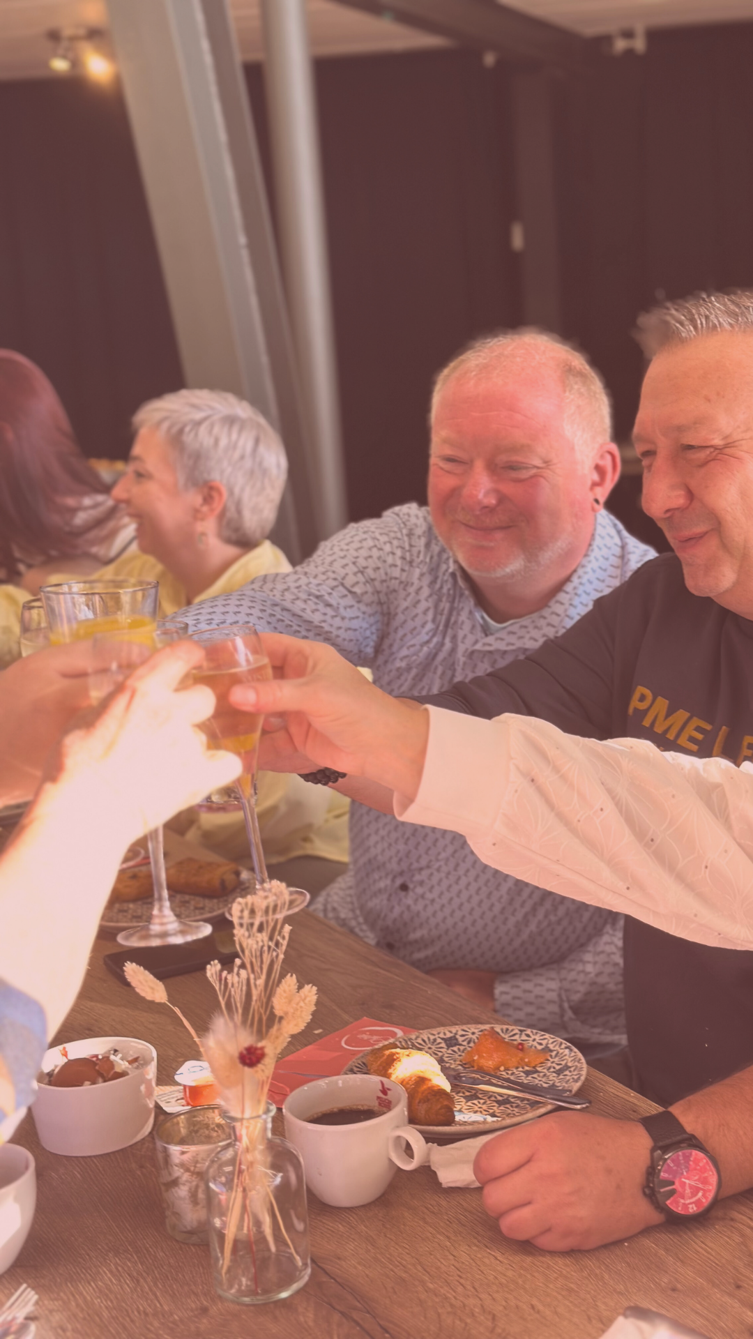 Gezellige restaurantsfeer met mensen die aan tafel zitten, toosten en genieten van koffie, gebak en andere gerechten.