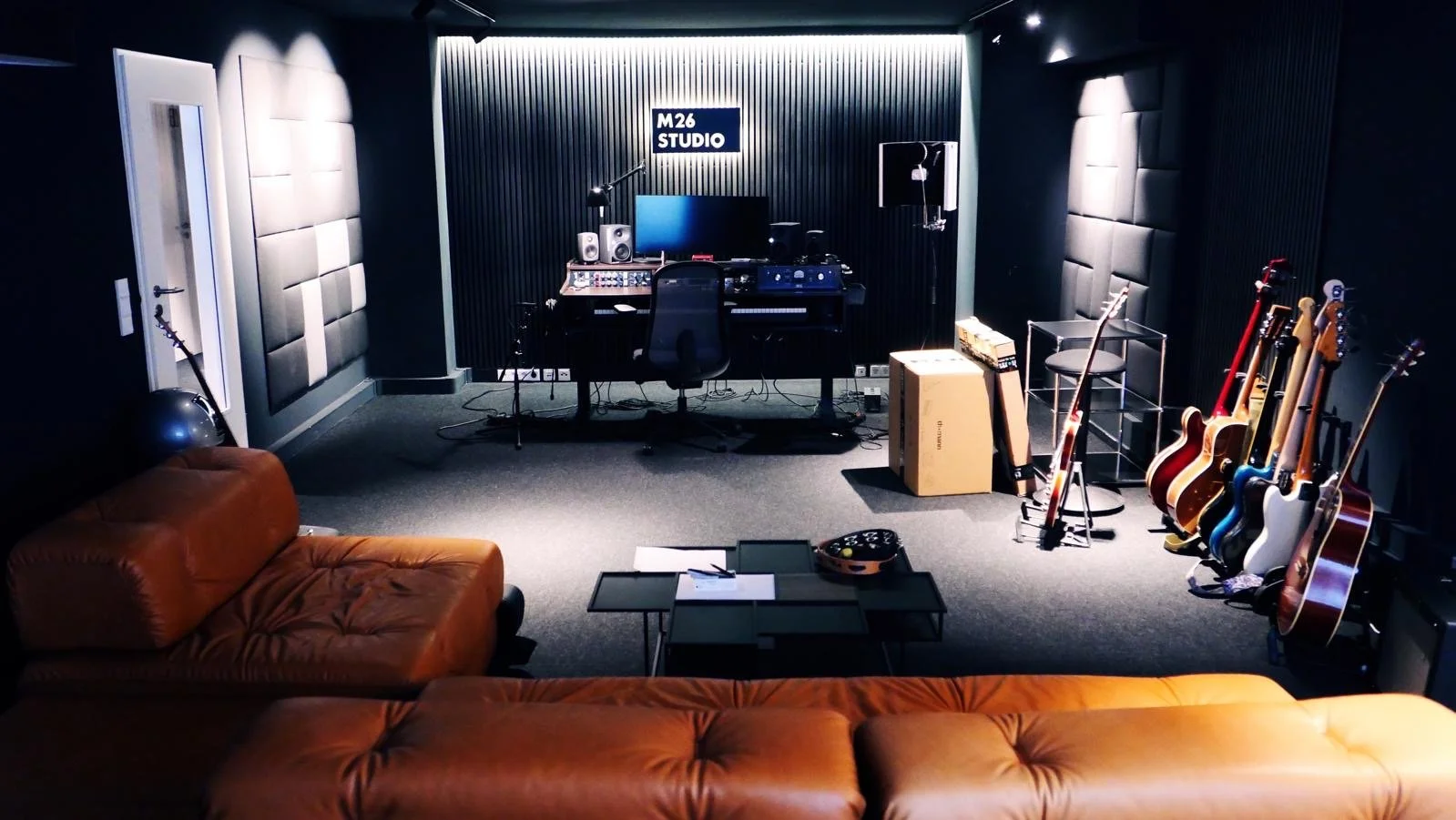 Musikstudio mit Gitarren, Sitzgelegenheiten, Aufnahmeausrüstung und einem Schreibtisch, Dekoration im schwarzen Raum.