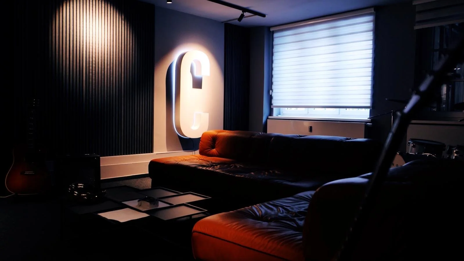 Beleuchteter Lichtbuchstabe in Form eines Ls an einer schwarzen Wand, mit Sofa, Couchtisch, Gitarre und Musikinstrumenten im modernen Wohnzimmer.