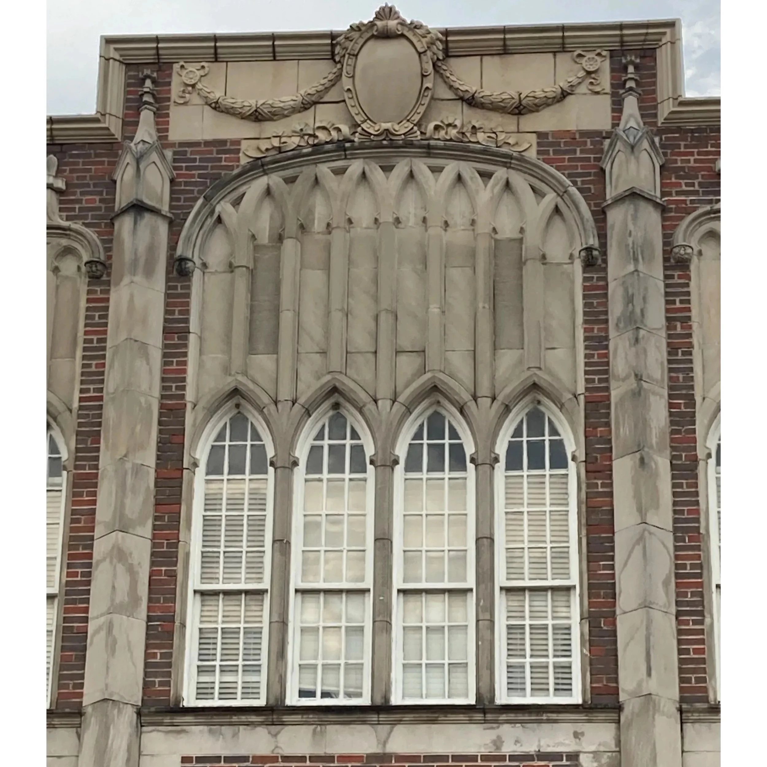 Close-up of a building facade of Capitol Heights Middle School with Gothic-style windows, stone detailing, and decorative elements on a brick and stone exterior.