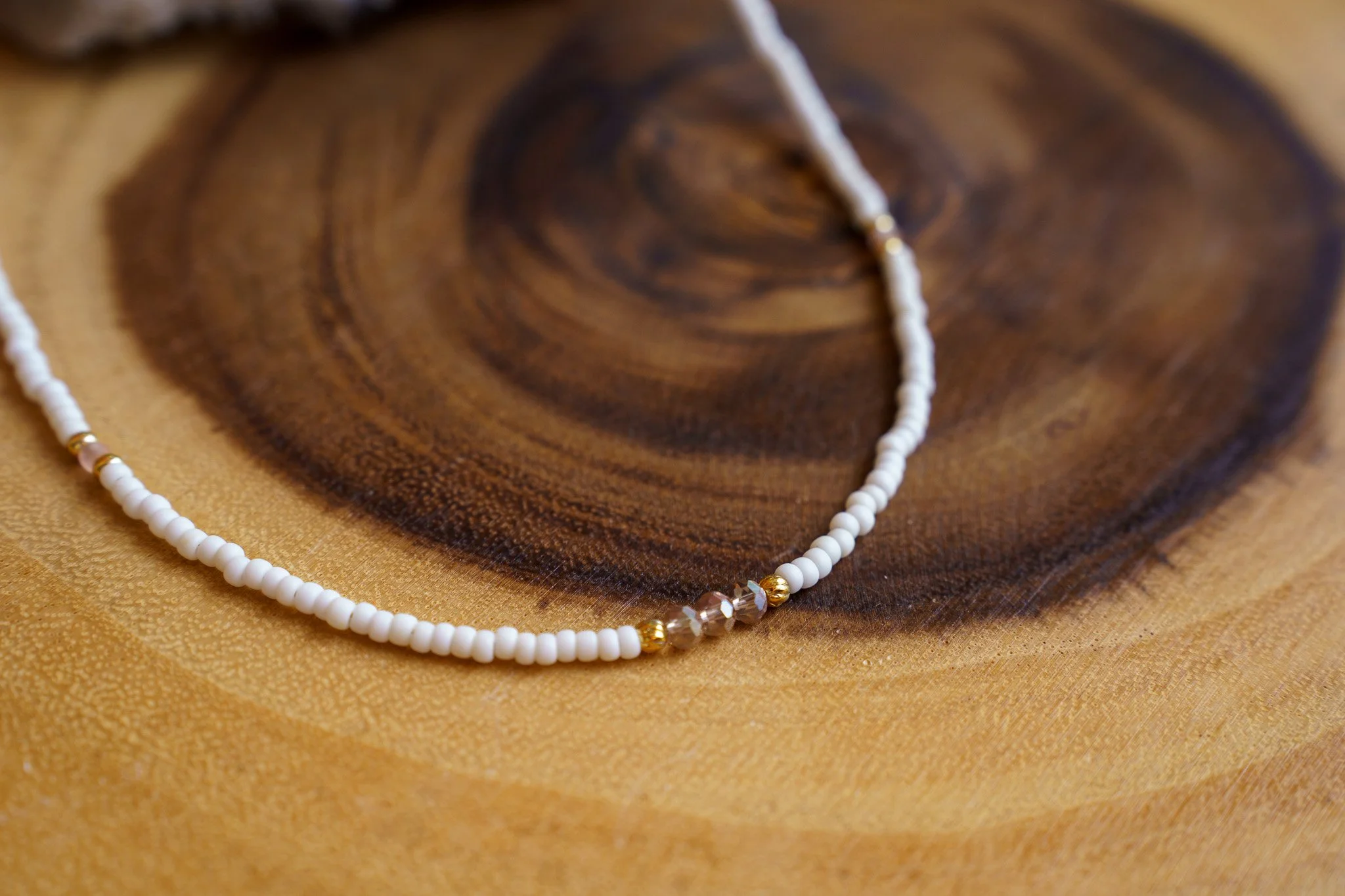 Handmade necklace with pink crystal beads, white seed beads, gold seed beads, and 18k gold PVD findings. Necklace measures approximately 16" with a 2" extender.