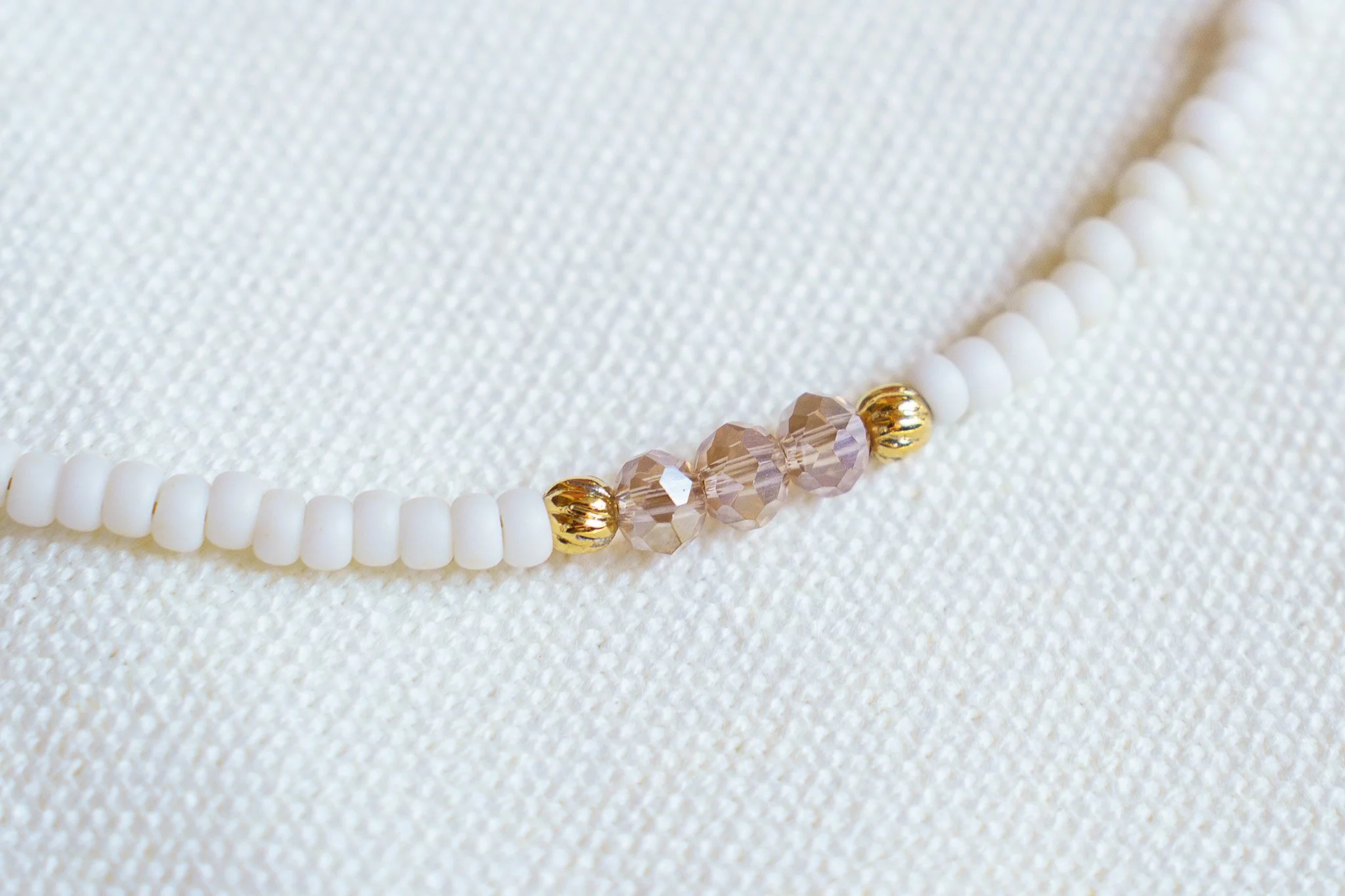 Handmade necklace with pink crystal beads, white seed beads, gold seed beads, and 18k gold PVD findings. Necklace measures approximately 16" with a 2" extender.