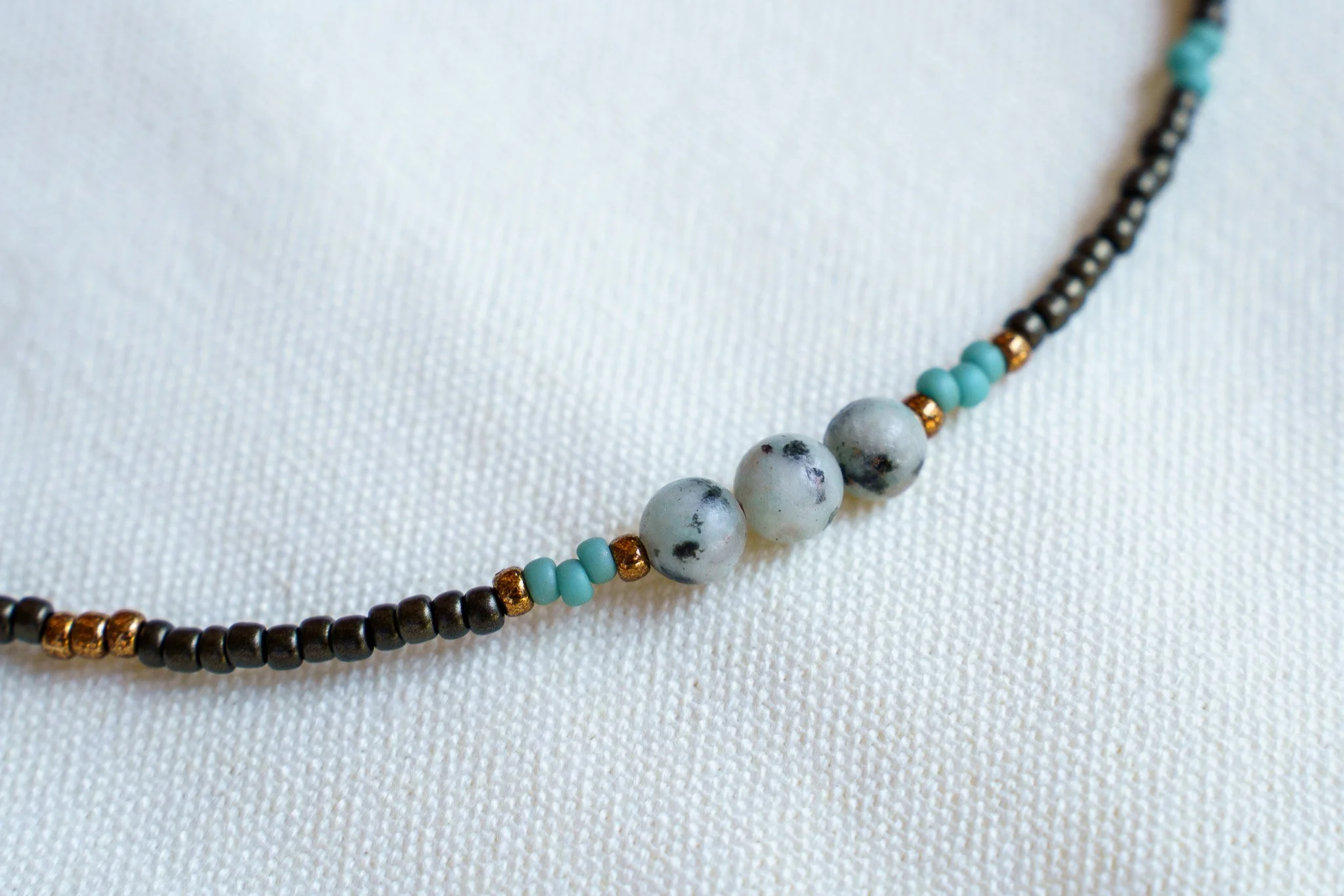 Handmade necklace with three kiwi jasper stones and black and bronze seed beads with 18k gold PVD findings. Necklace measures approximately 16" with a 2" extender.