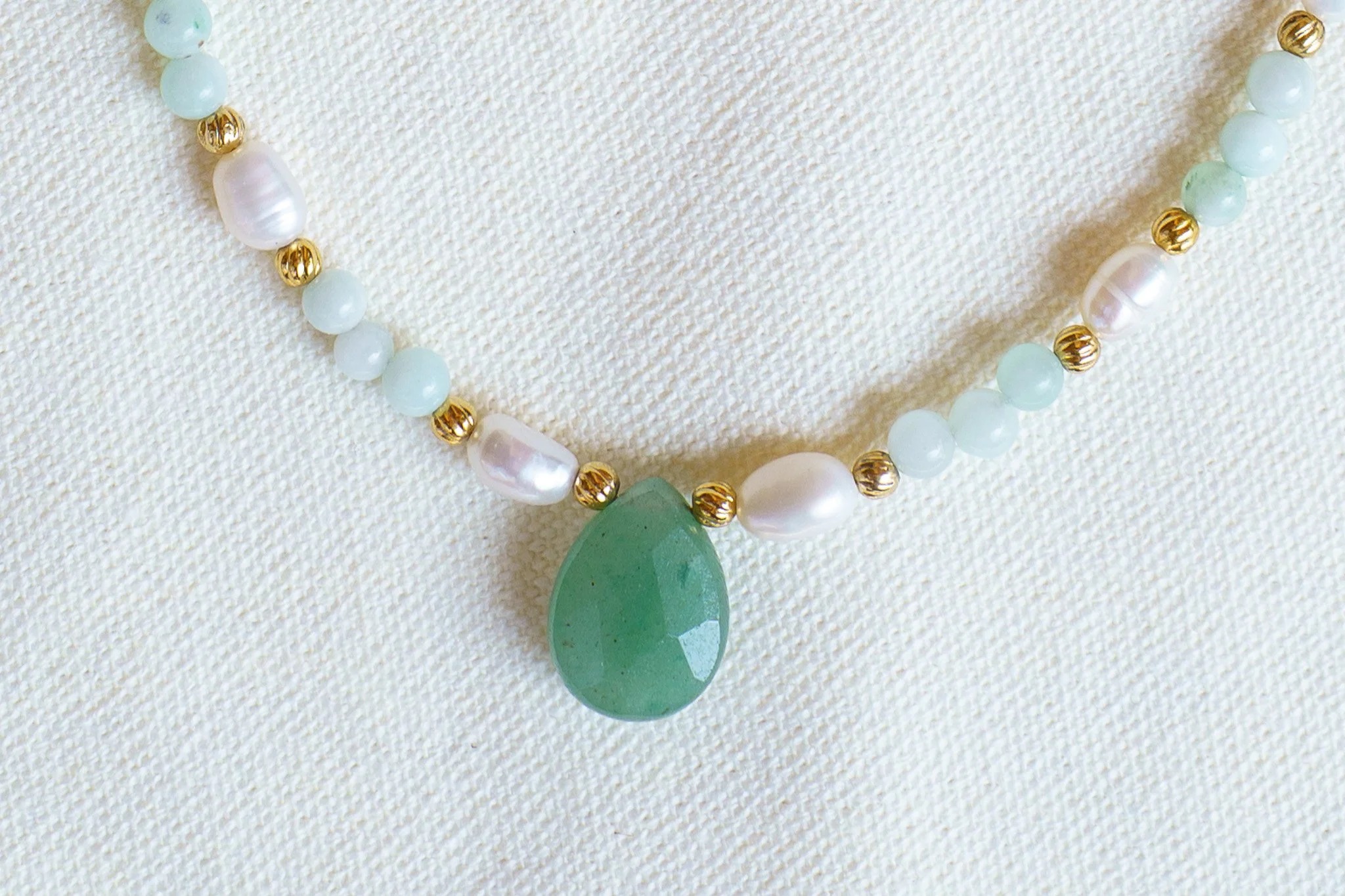 Handmade necklace with amazonite beads, freshwater pearls, and a green aventurine pendant with gold seed beads and 18k gold PVD findings. Necklace measures approximately 15" with a 2" extender.