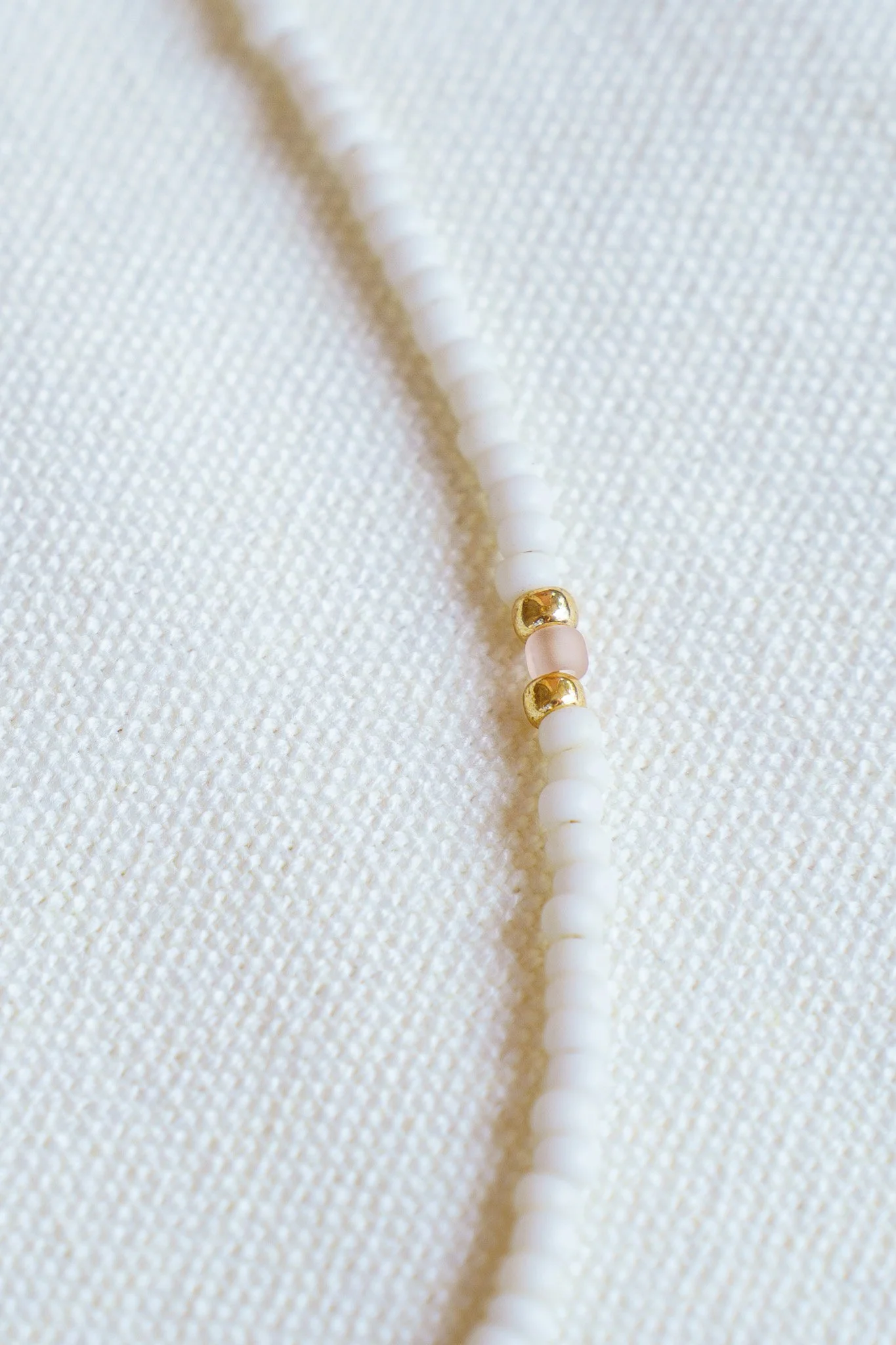 Handmade necklace with pink crystal beads, white seed beads, gold seed beads, and 18k gold PVD findings. Necklace measures approximately 16" with a 2" extender.