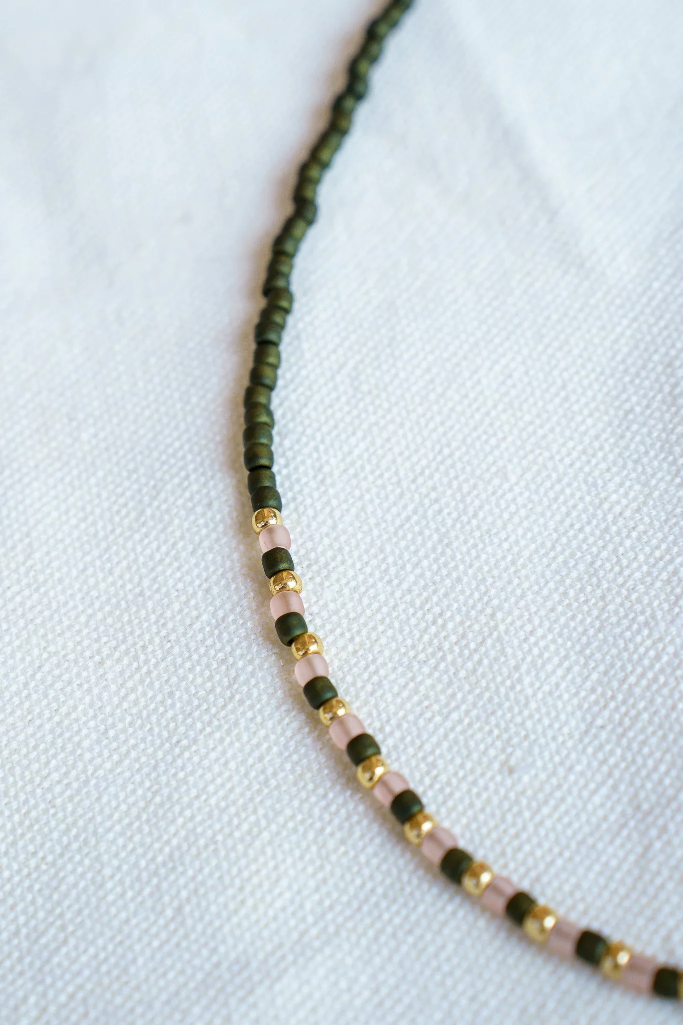 Handmade green, pink, and gold seed bead necklace with 18k gold PVD findings. Necklace measures approximately 16" with a 2" extender.