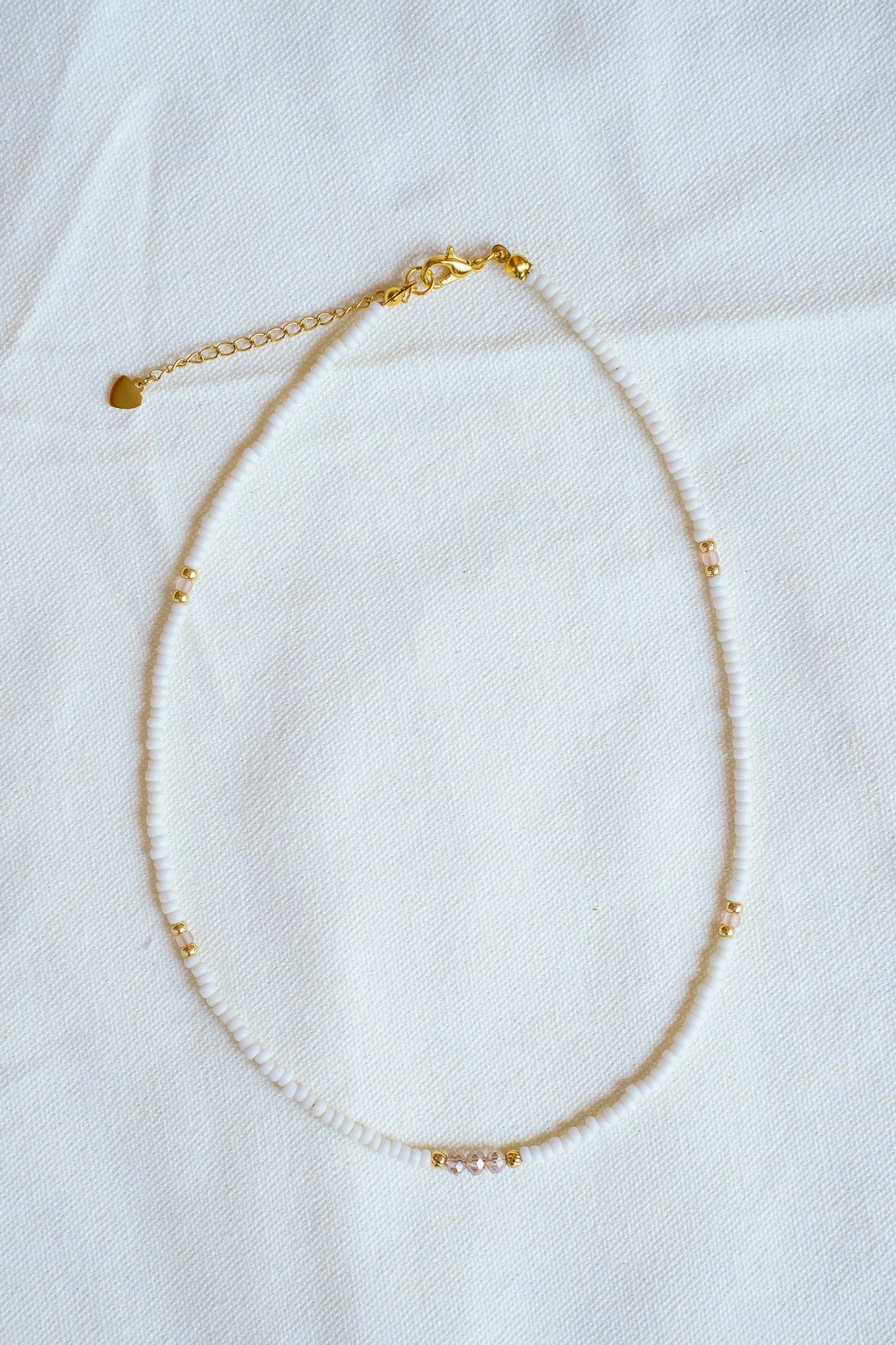 Handmade necklace with pink crystal beads, white seed beads, gold seed beads, and 18k gold PVD findings. Necklace measures approximately 16" with a 2" extender.