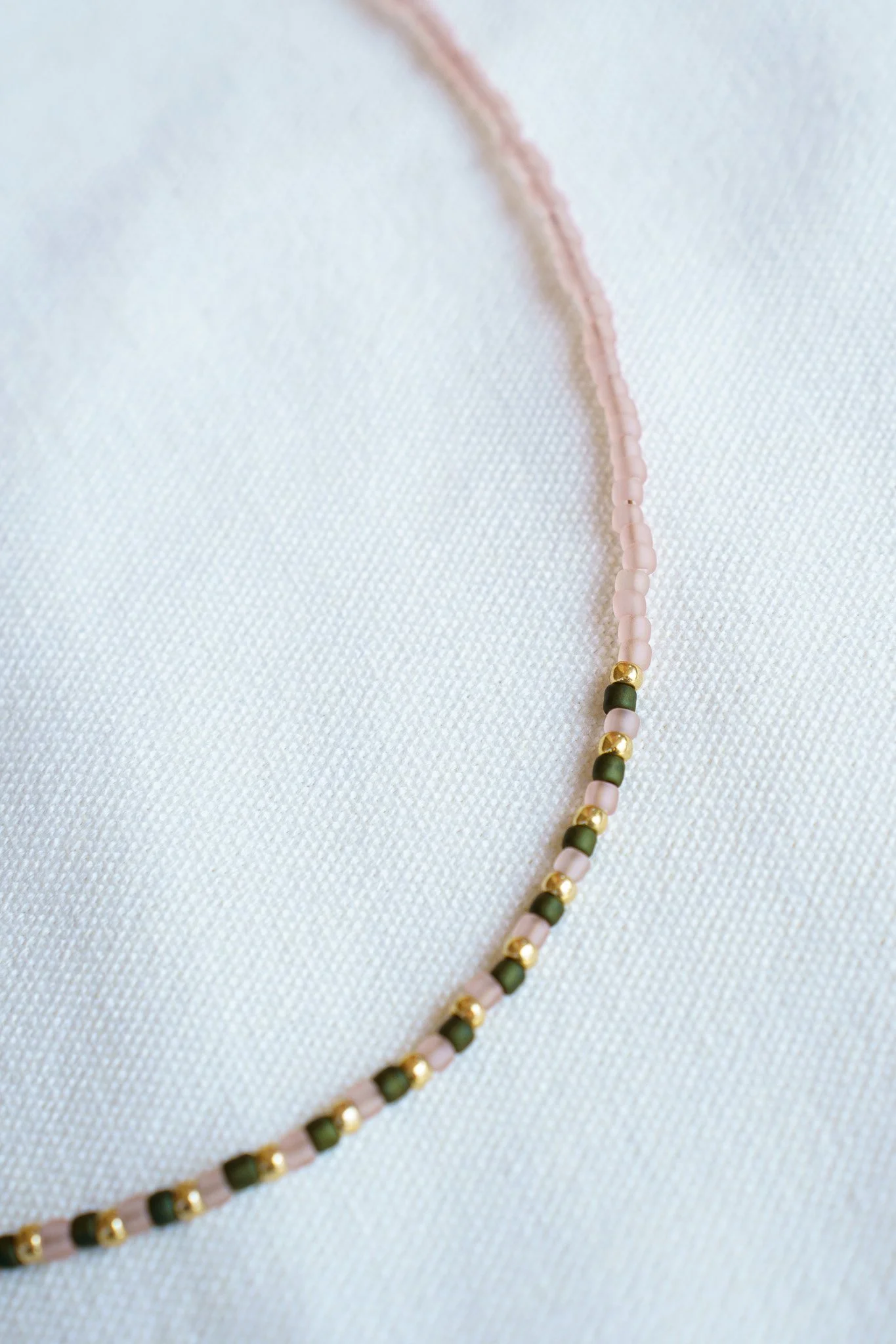 Handmade green, pink, and gold seed bead necklace with 18k gold PVD findings. Necklace measures approximately 16" with a 2" extender.