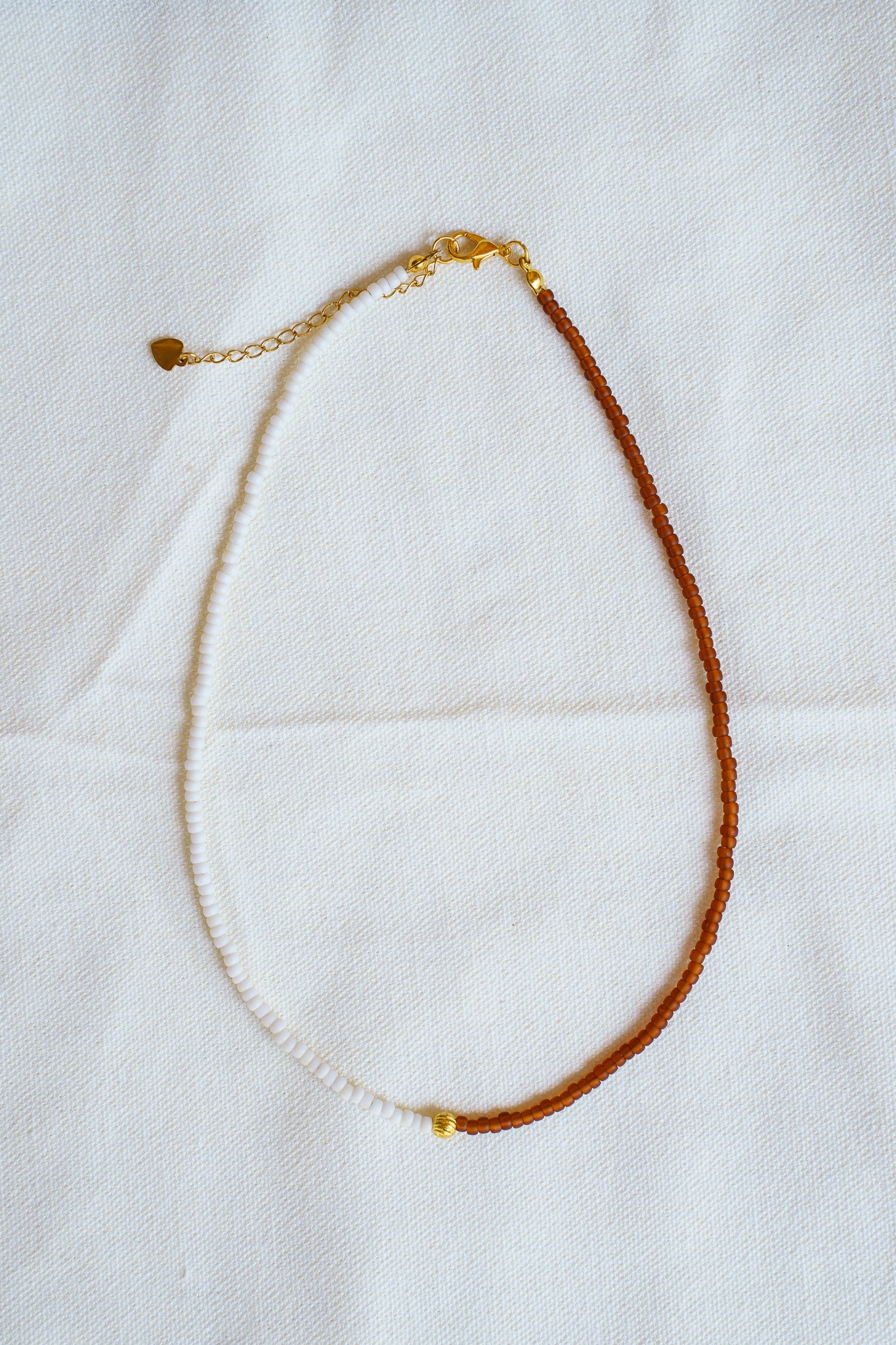 Handmade necklace with white, rust brown, and gold seed beads and with 18k gold PVD findings. Necklace measures approximately 16" with a 2" extender.