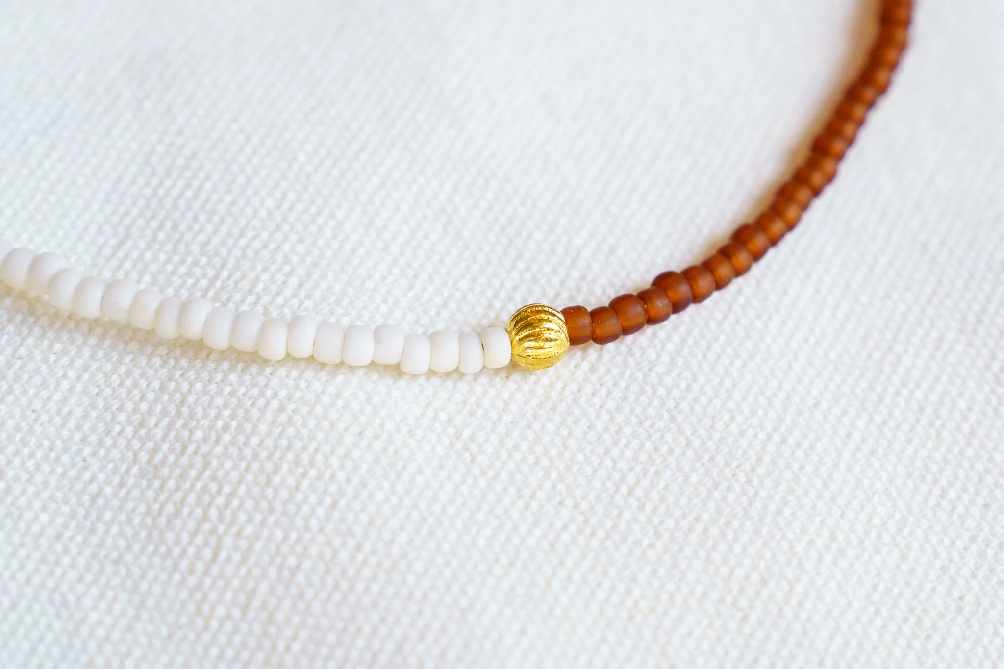 Handmade necklace with white, rust brown, and gold seed beads and with 18k gold PVD findings. Necklace measures approximately 16" with a 2" extender.