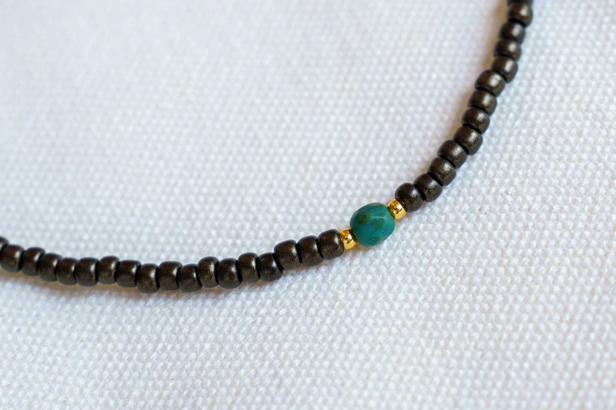 Handmade necklace with teal accent beads and black and gold seed beads with 18k gold PVD findings. Necklace measures approximately 17" with a 2" extender.