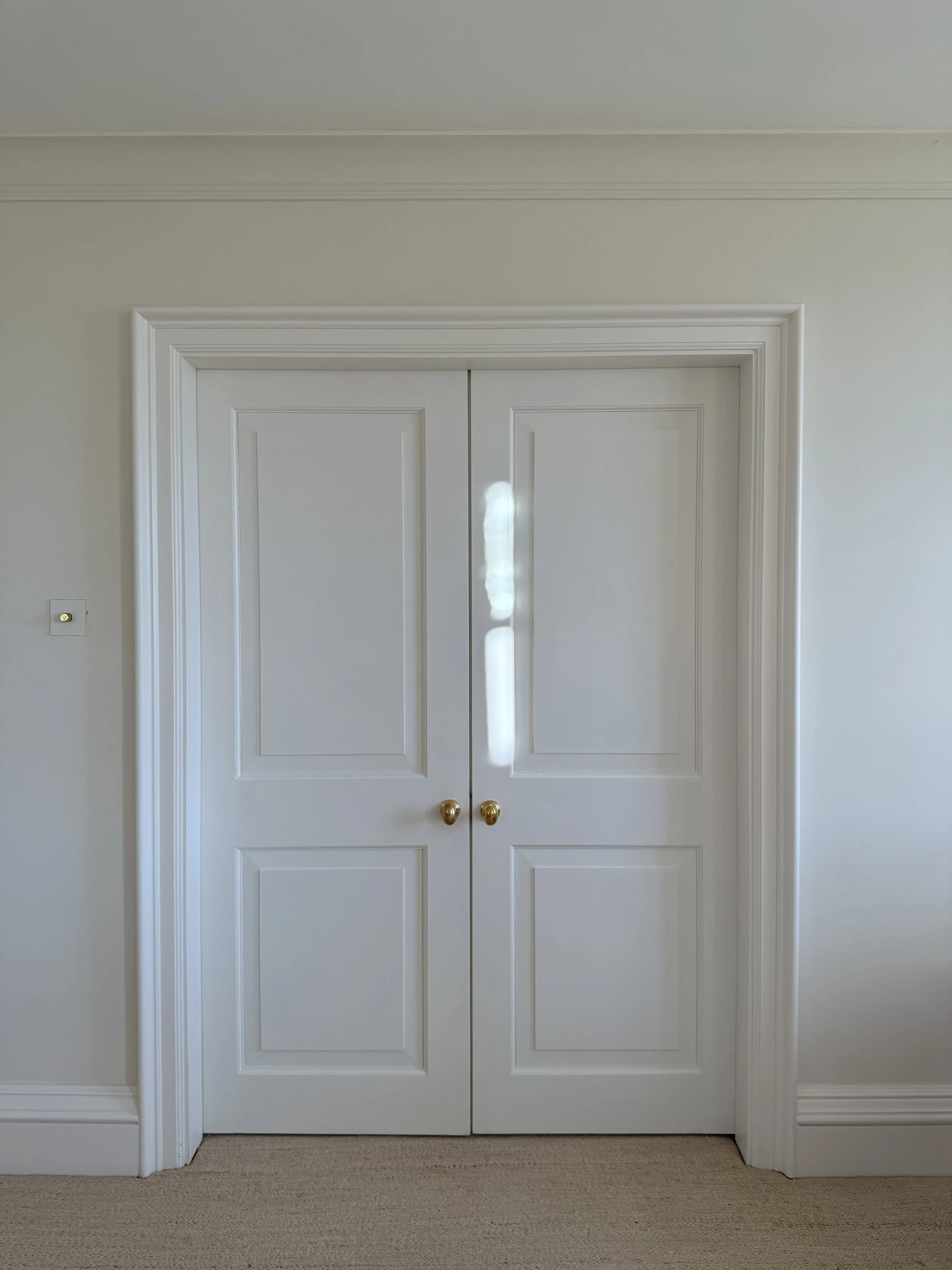 White double doors with gold knobs in a room with white walls and beige carpet.