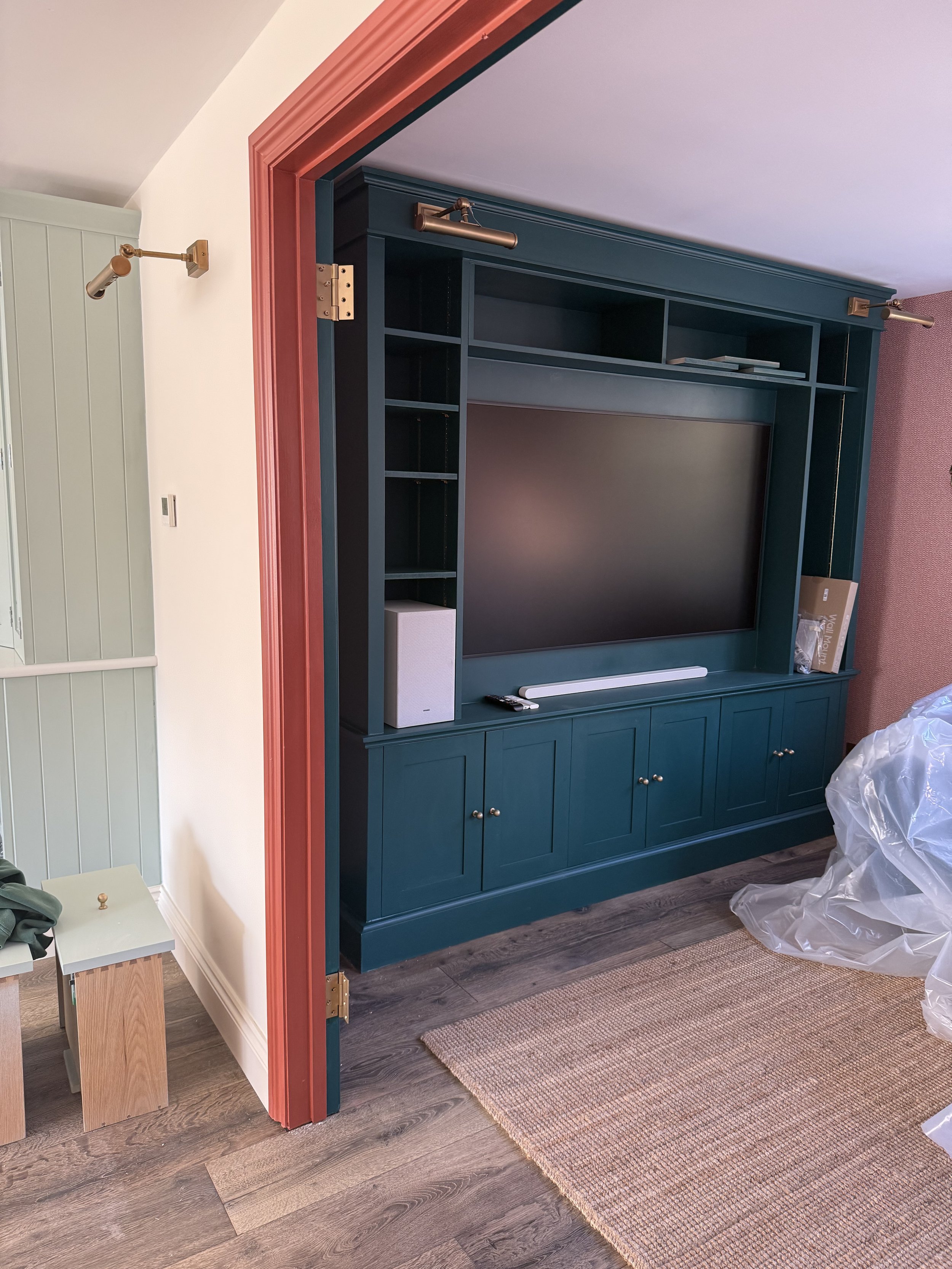 A teal entertainment center with a television mounted on it, surrounded by open shelving and closed cabinet doors, in a living room with wood flooring and a beige rug.