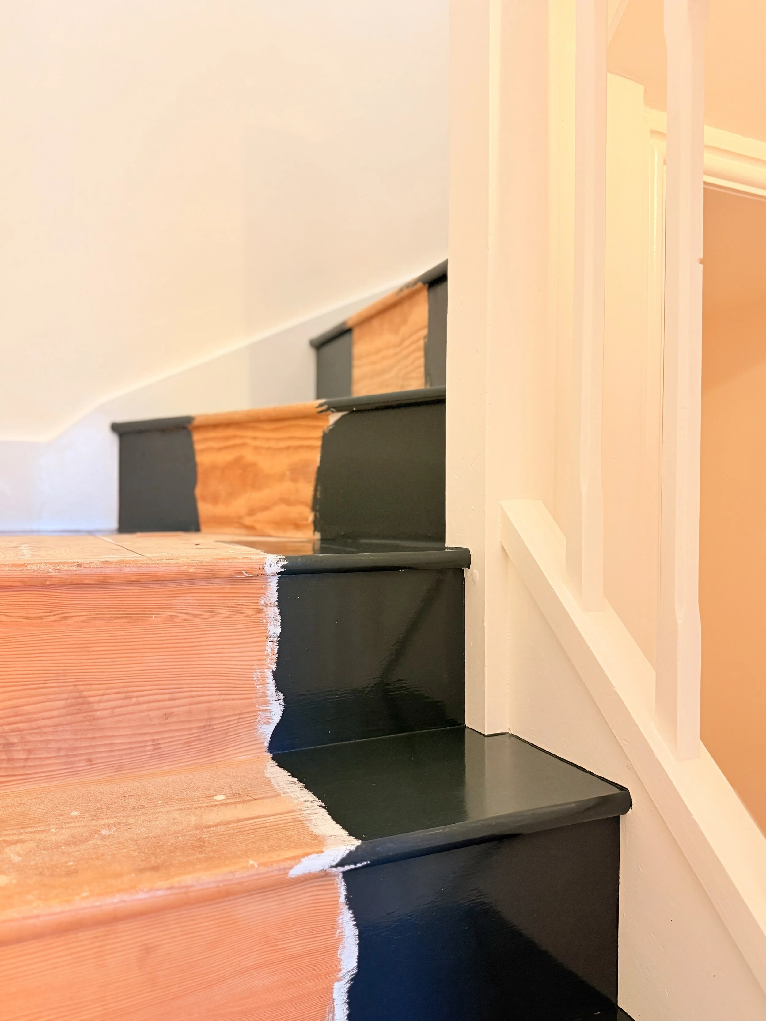 Close-up of staircase with partially painted black risers and unpainted wood treads, showing the painting process in progress.